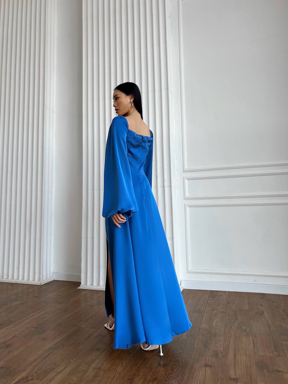 Woman in a blue dress standing against a white paneled wall.