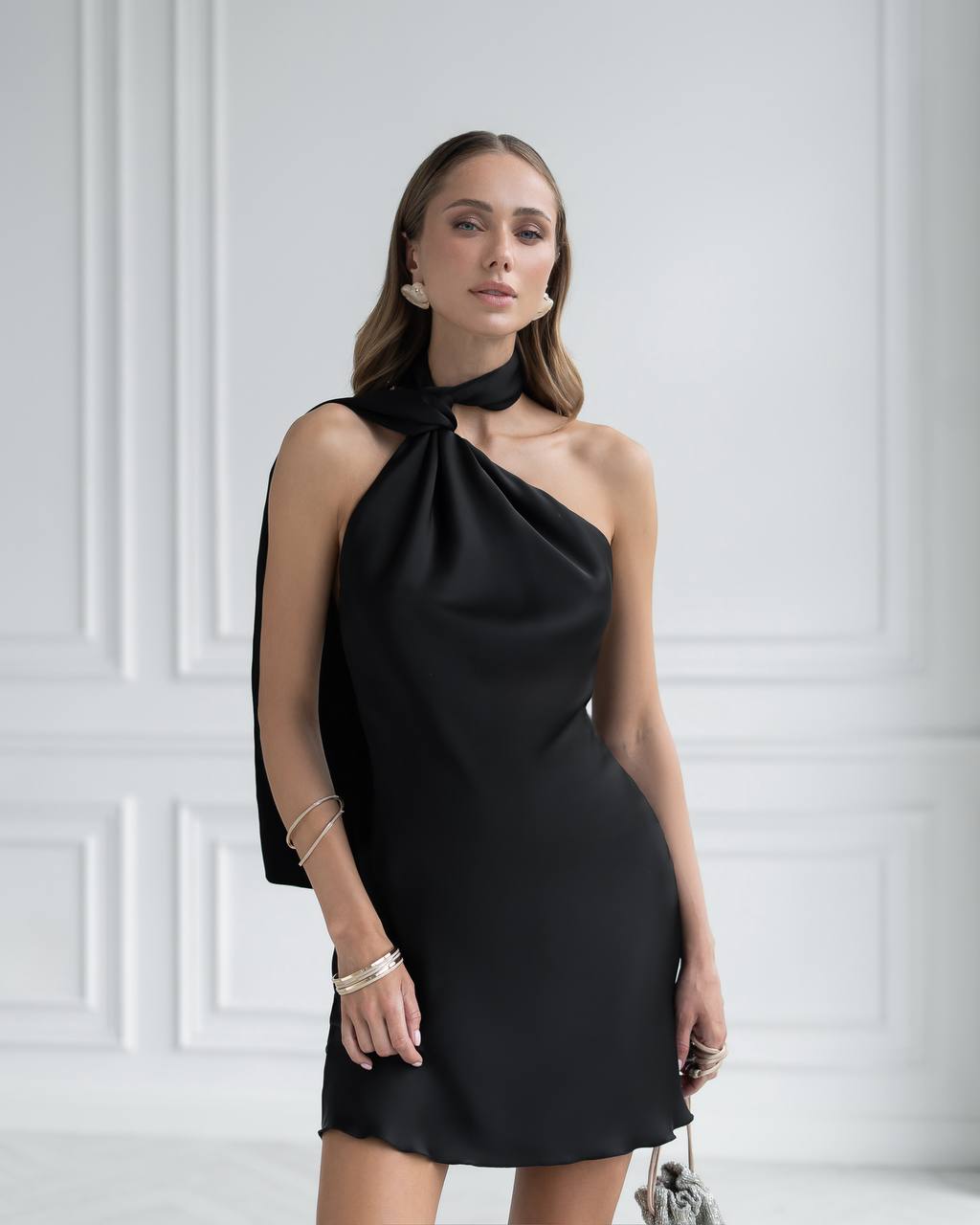 Woman wearing a black one-shoulder dress against a white wall