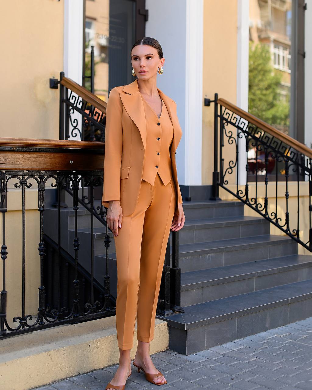 Woman in a mustard yellow suit standing on steps outside a building.