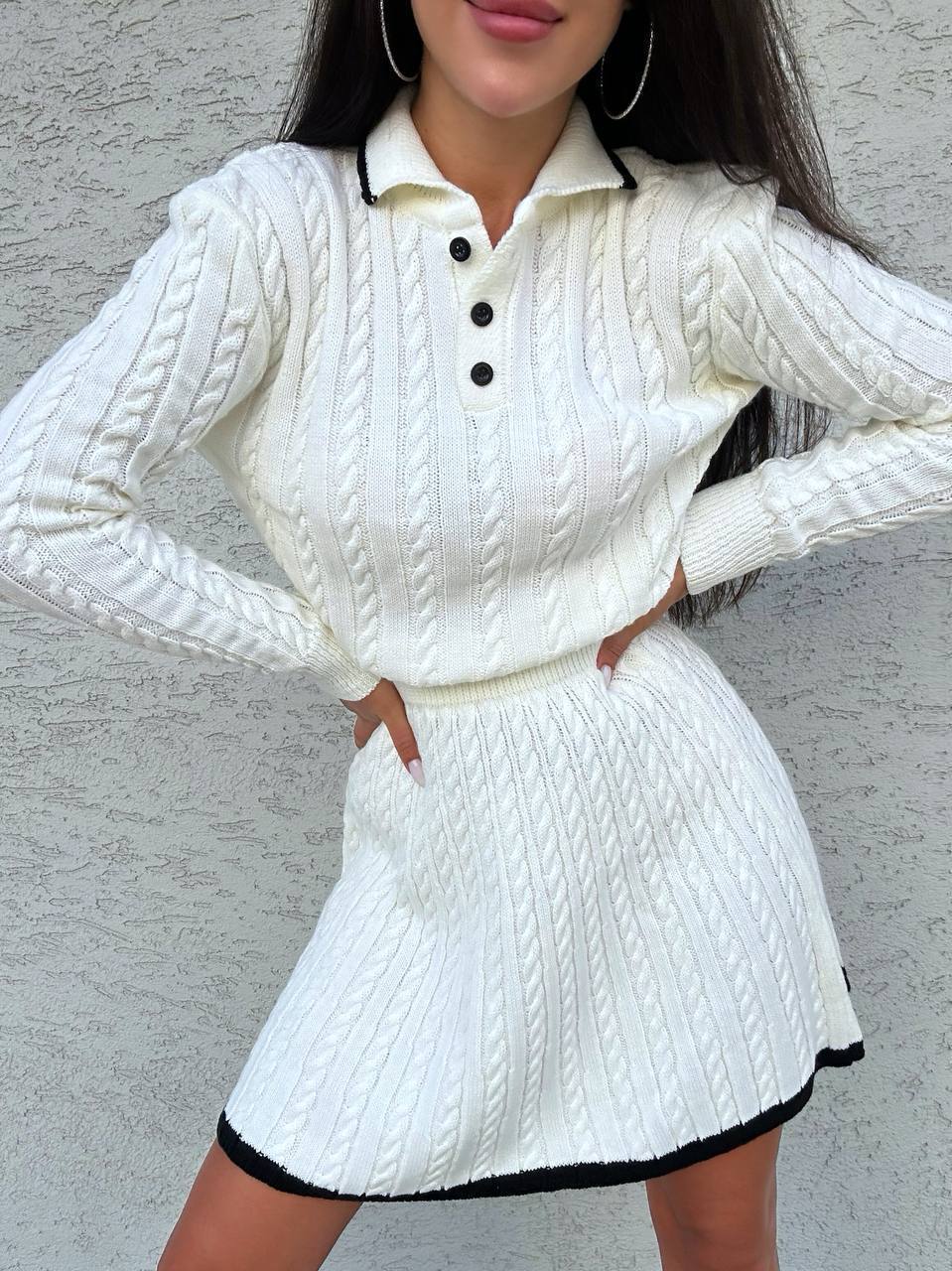 Person wearing a white cable knit outfit with black accents against a gray background