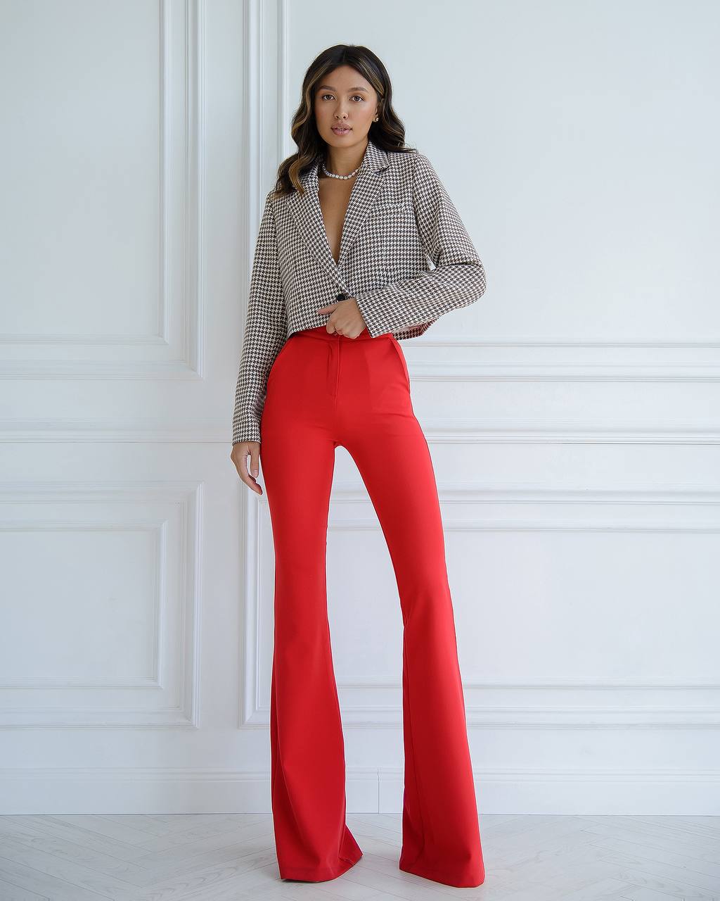 Woman wearing a checkered blazer and red pants against a white wall
