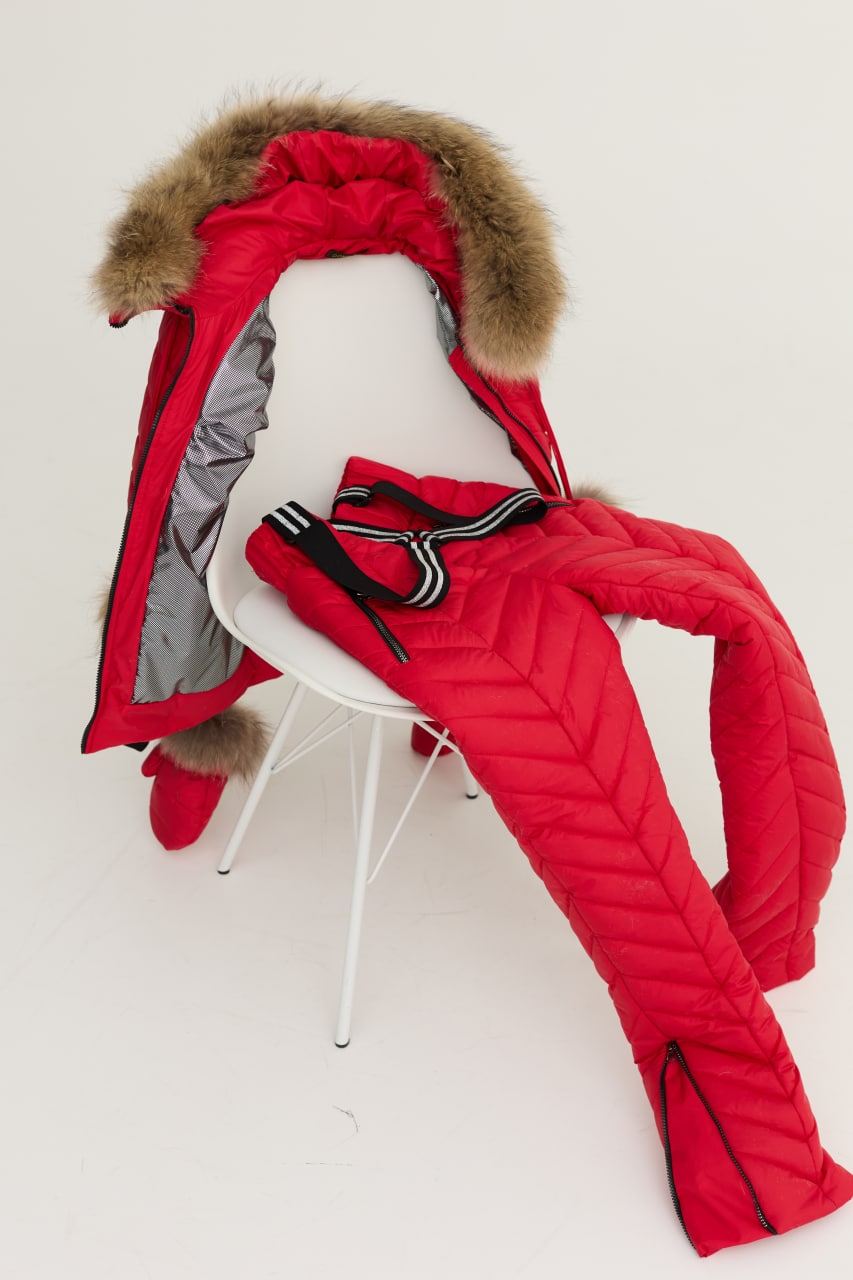 Red winter coat with fur hood and matching mittens on a white chair against a white background