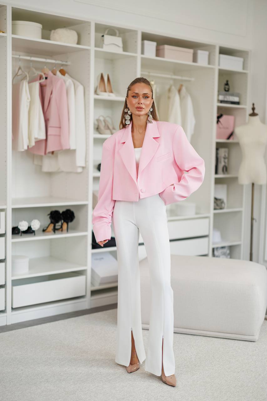 Woman in a pink jacket and white pants standing in a stylishly organized closet.