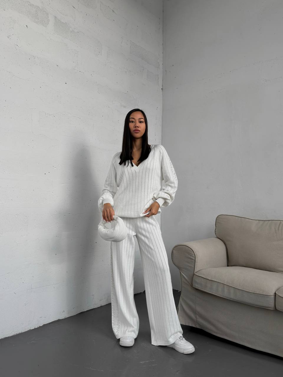 Woman in a white outfit standing in a minimalistic room with a gray sofa.