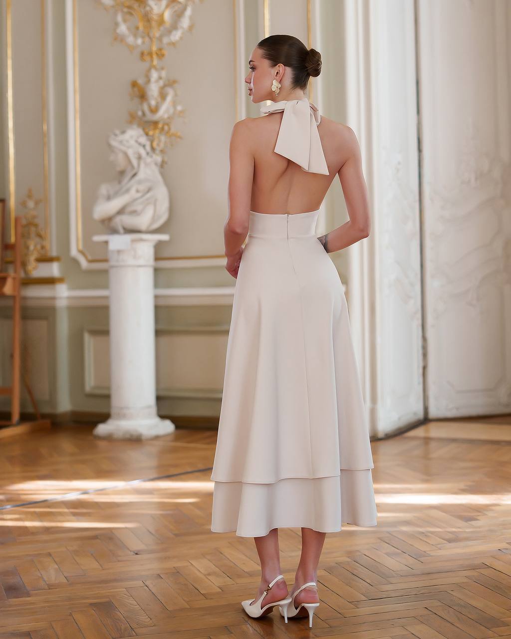 Woman in a white dress standing in an elegant room with classical decor.