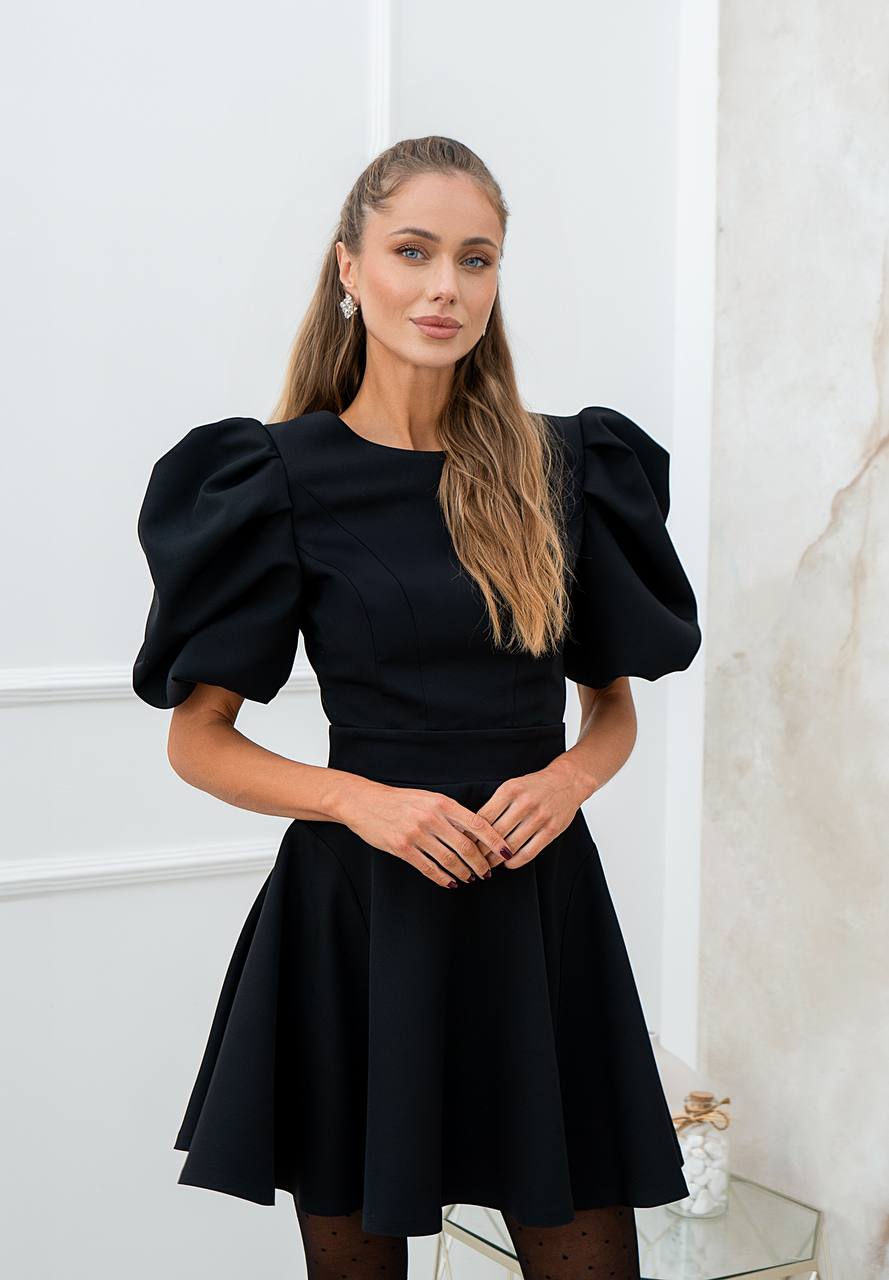 Woman wearing a black dress with puff sleeves in an elegant interior setting
