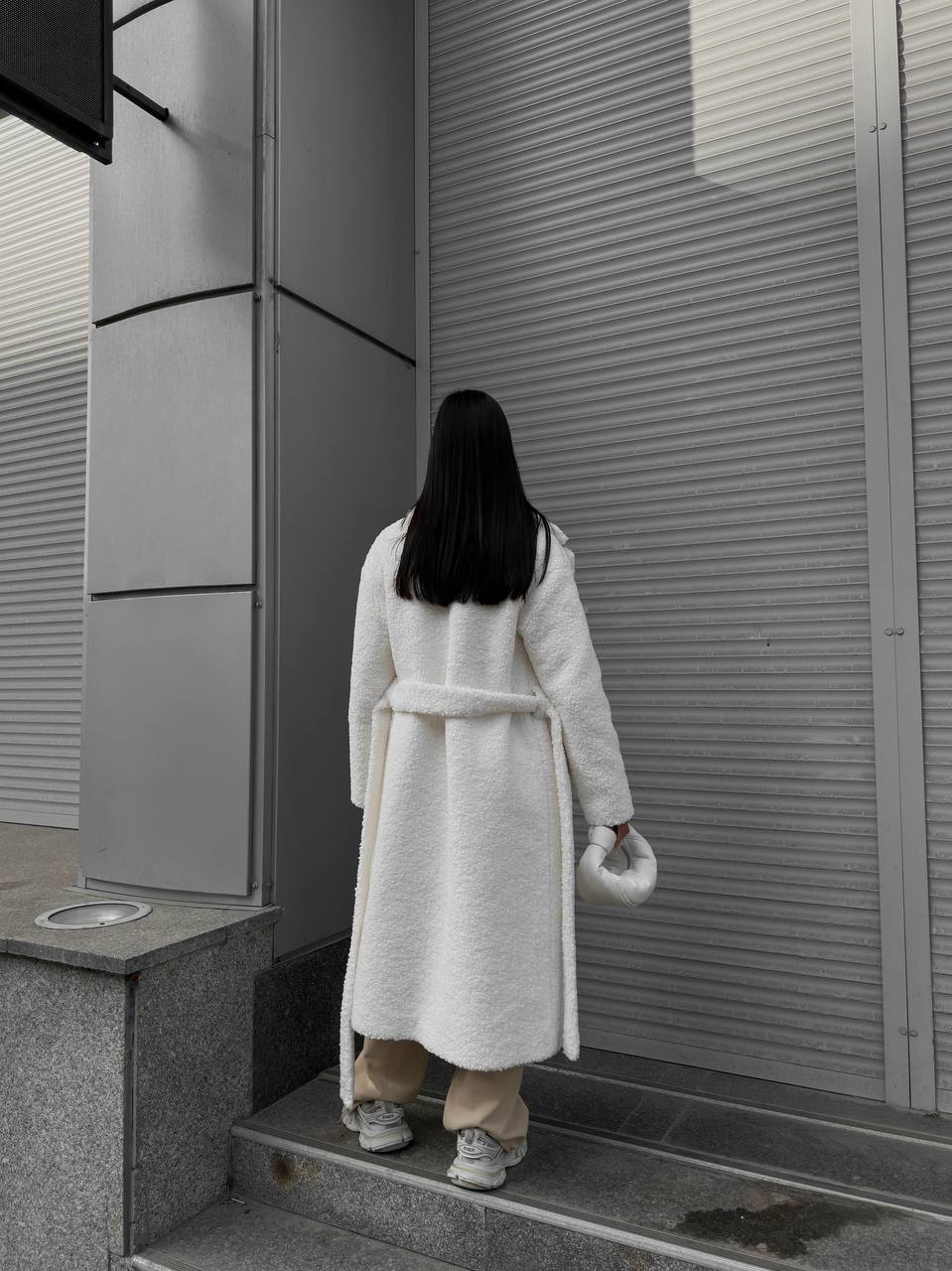 Person in a long coat walking up steps in an urban setting