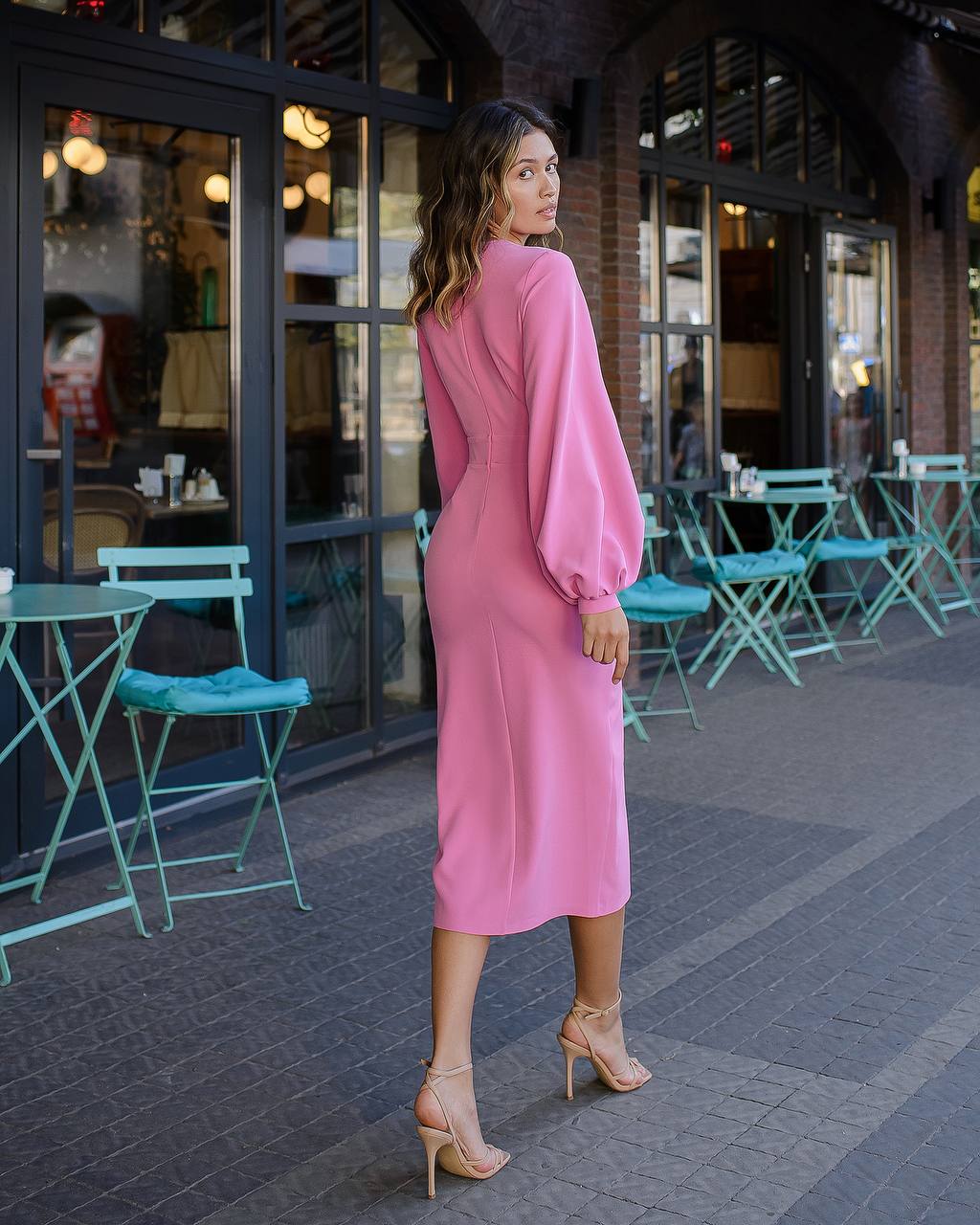 Woman in a pink dress standing on a sidewalk with outdoor seating in the background