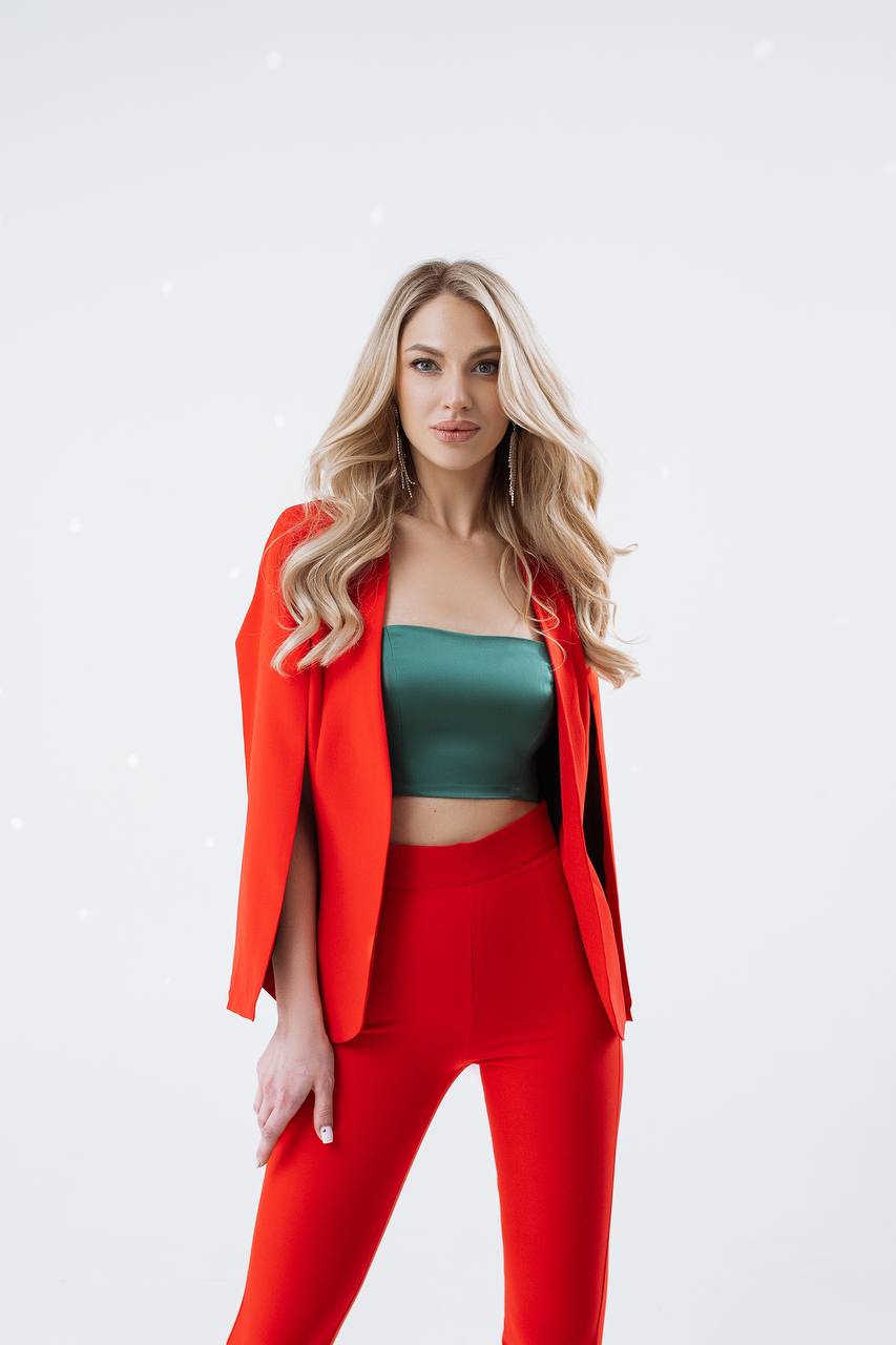 Woman wearing a red blazer and pants with a green top on a white background