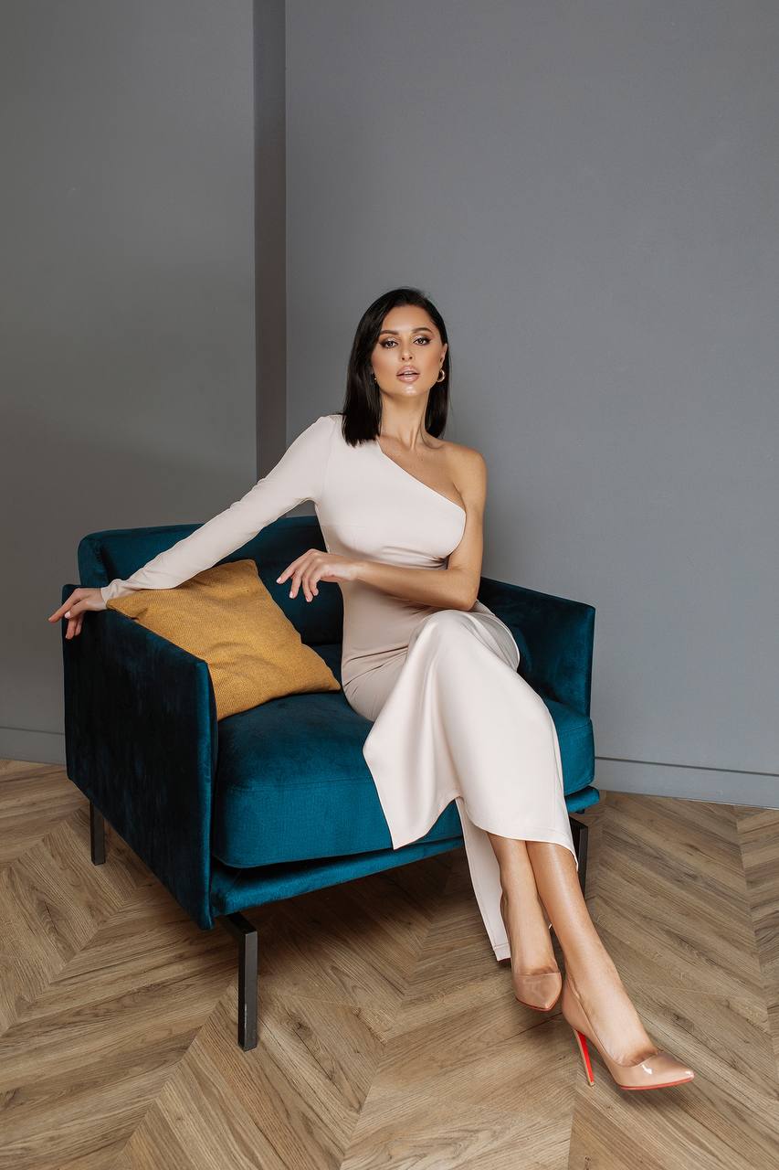 Woman in a white dress sitting on a blue chair with a gray wall background