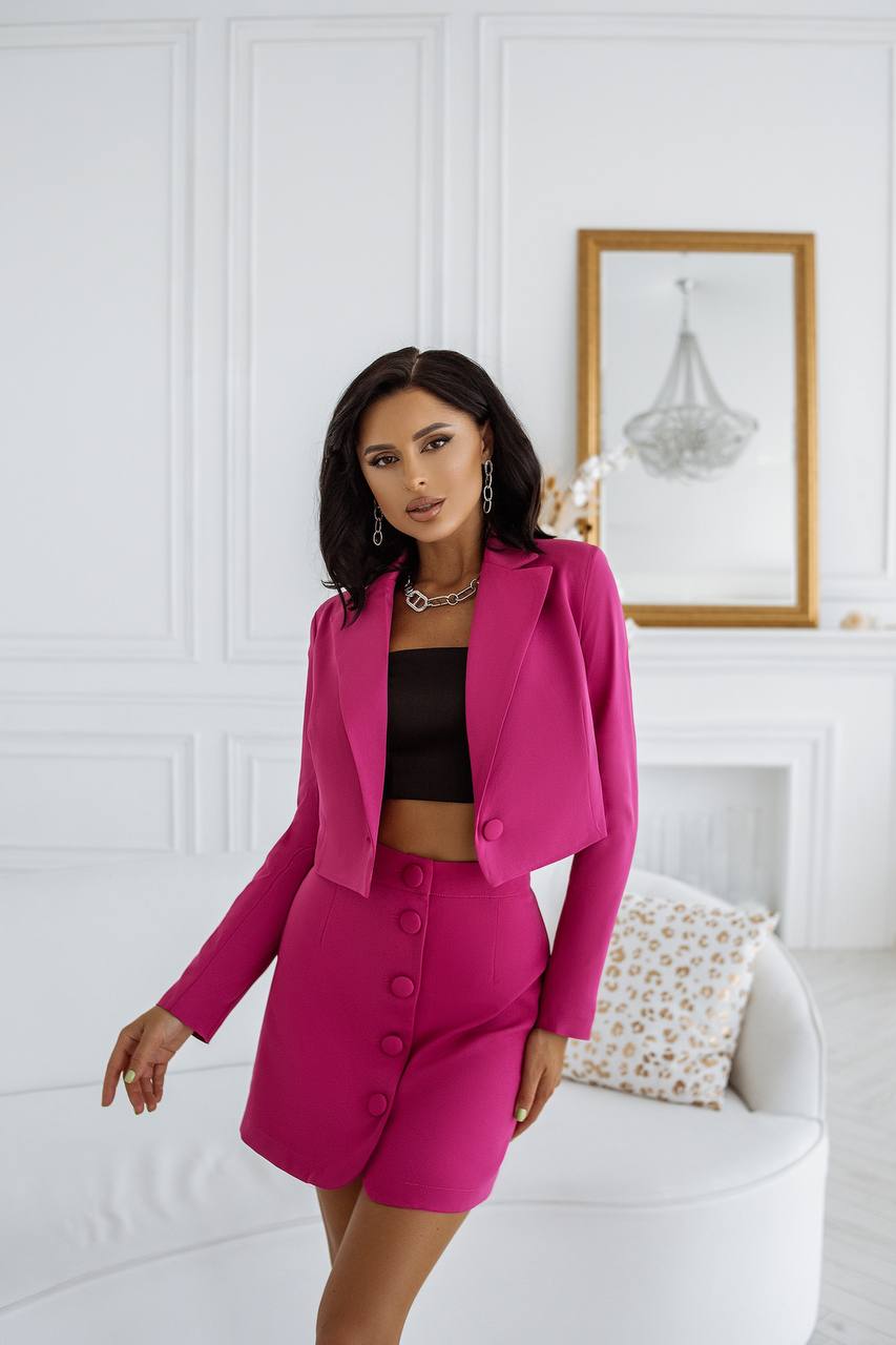 Woman in a pink suit standing in a stylish room with white walls and decor.