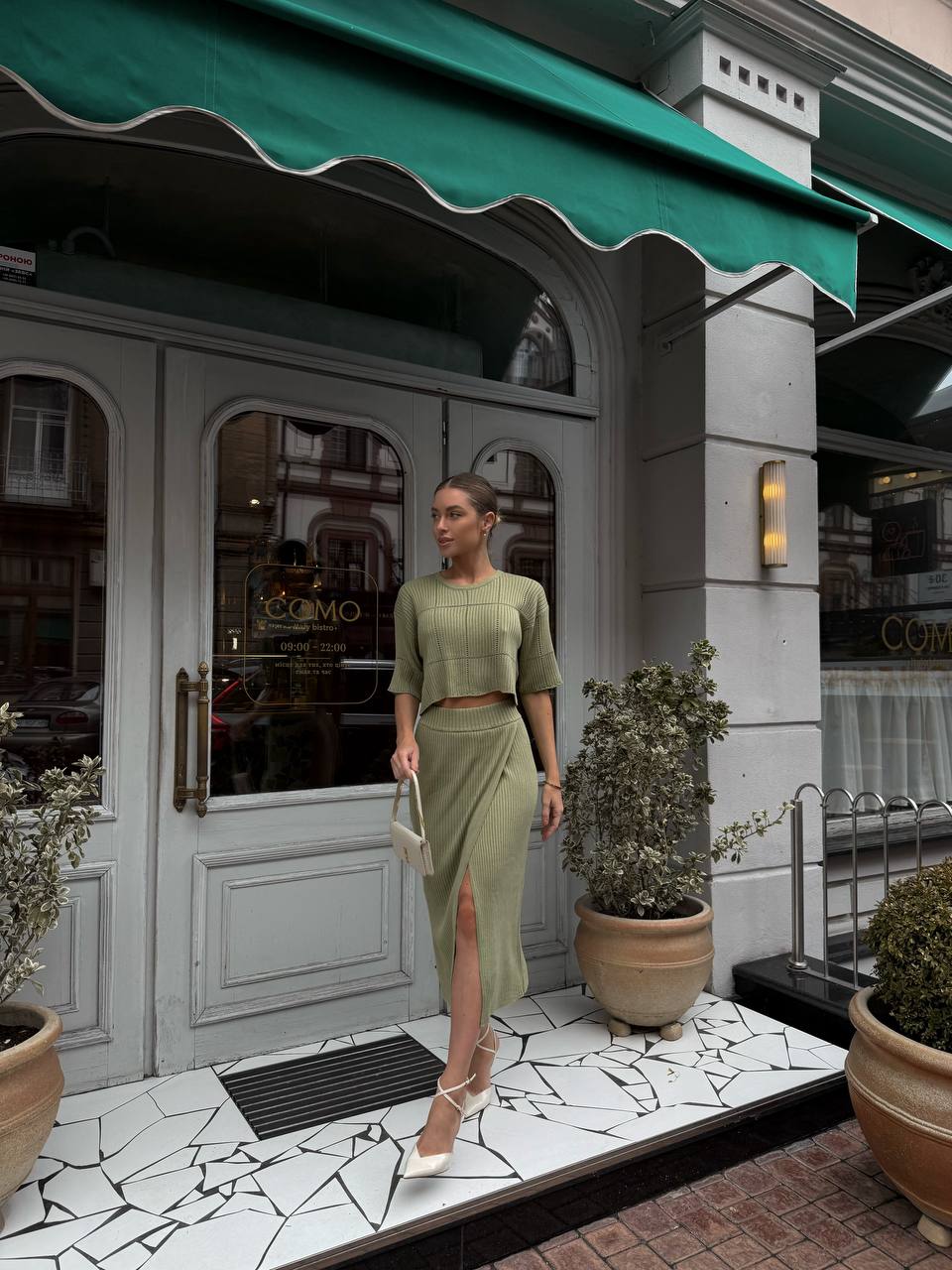 Woman in a green outfit standing in front of a store with a green awning.