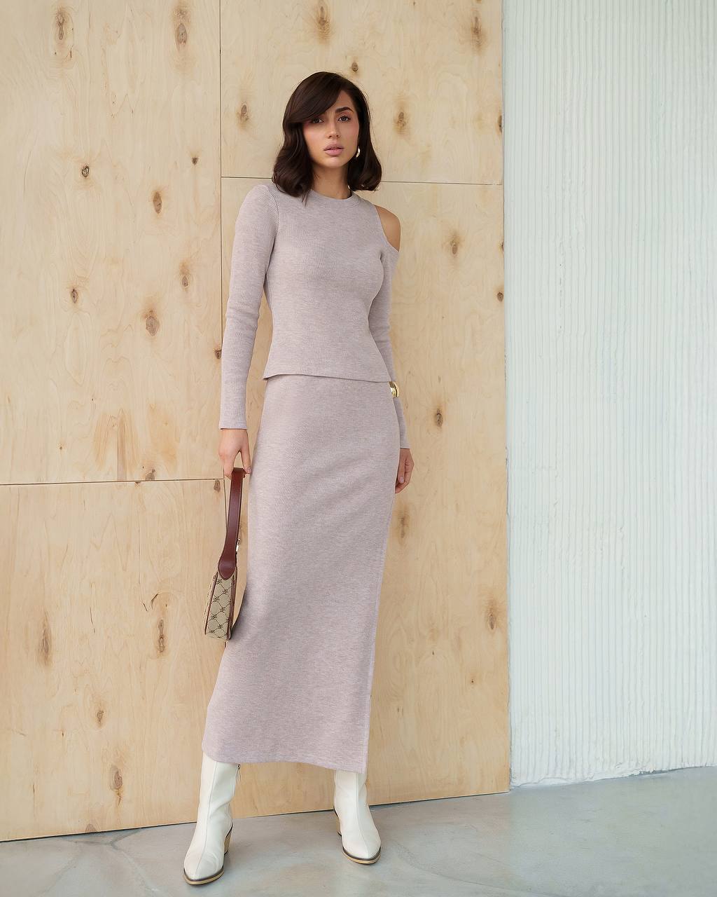 Woman wearing a light gray outfit standing against a wooden wall.