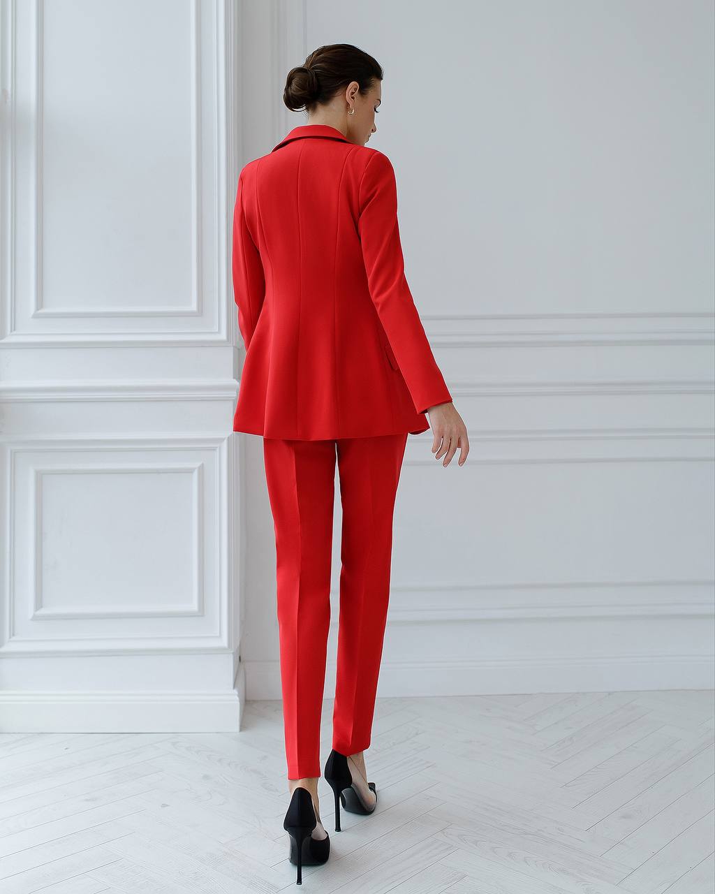 Woman wearing a red suit standing against a white wall.