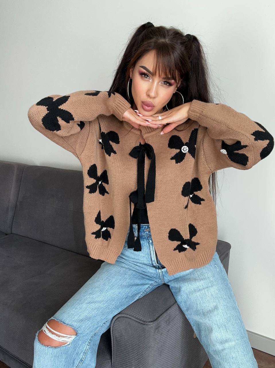 Woman wearing a brown cardigan with black butterfly patterns sitting on a gray couch.