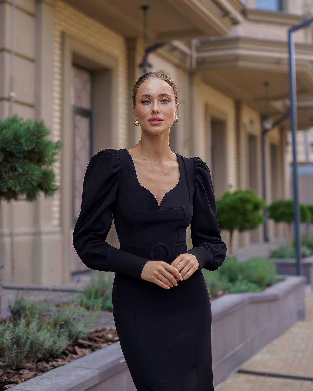 Woman in a black dress standing in front of a building with greenery