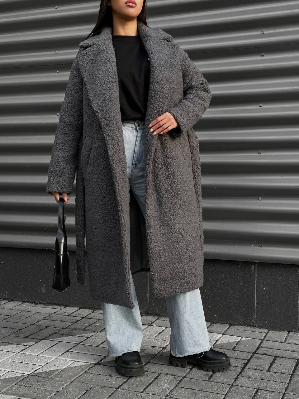 Person wearing a long gray coat with a neutral background