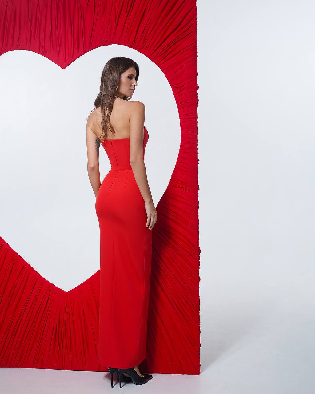 Woman in a red dress standing in front of a large heart-shaped cutout on a white background