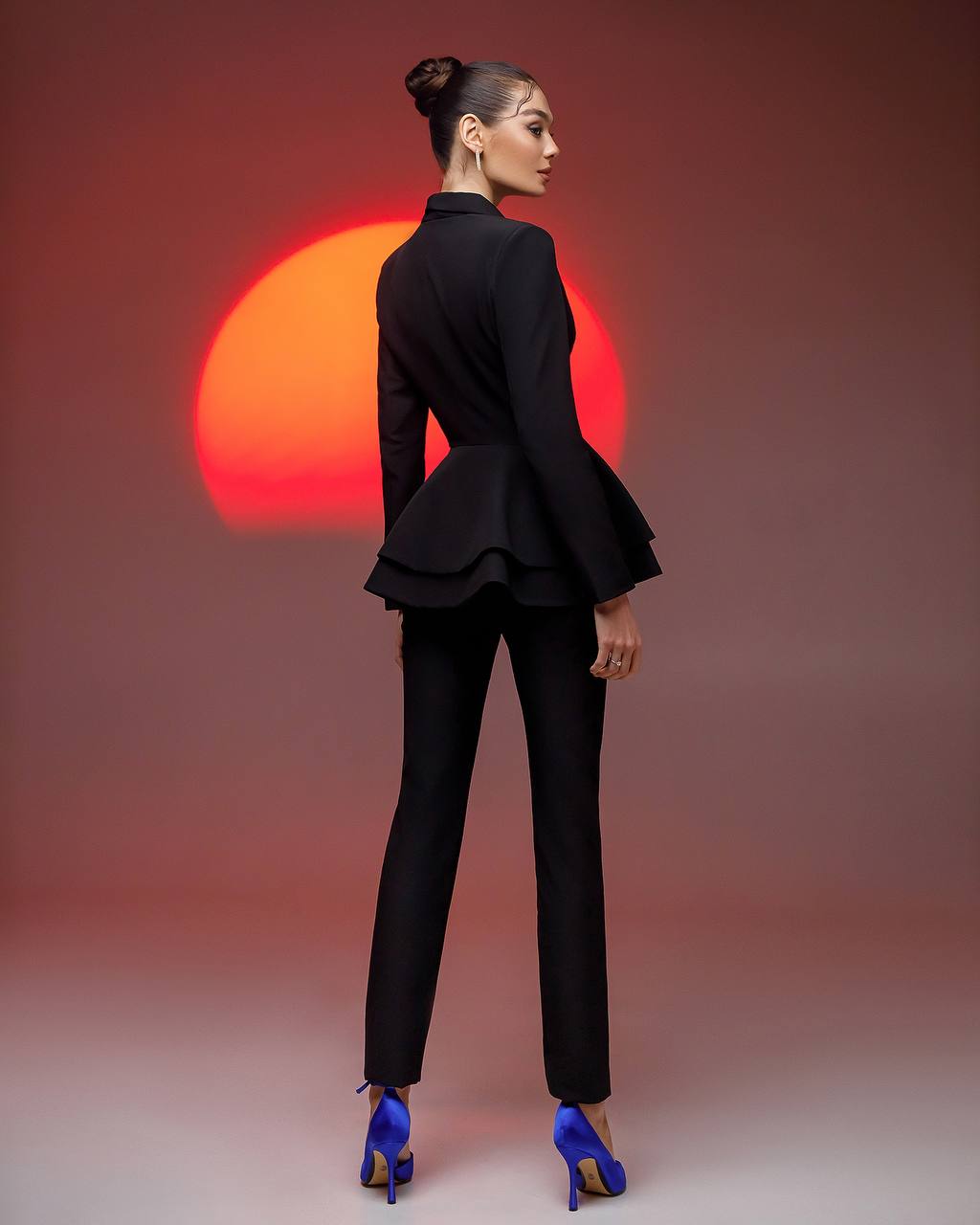 Woman in a black suit with peplum top against a red sun backdrop