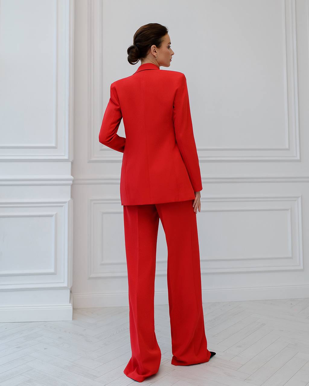 Woman wearing a red suit standing against a white paneled wall.