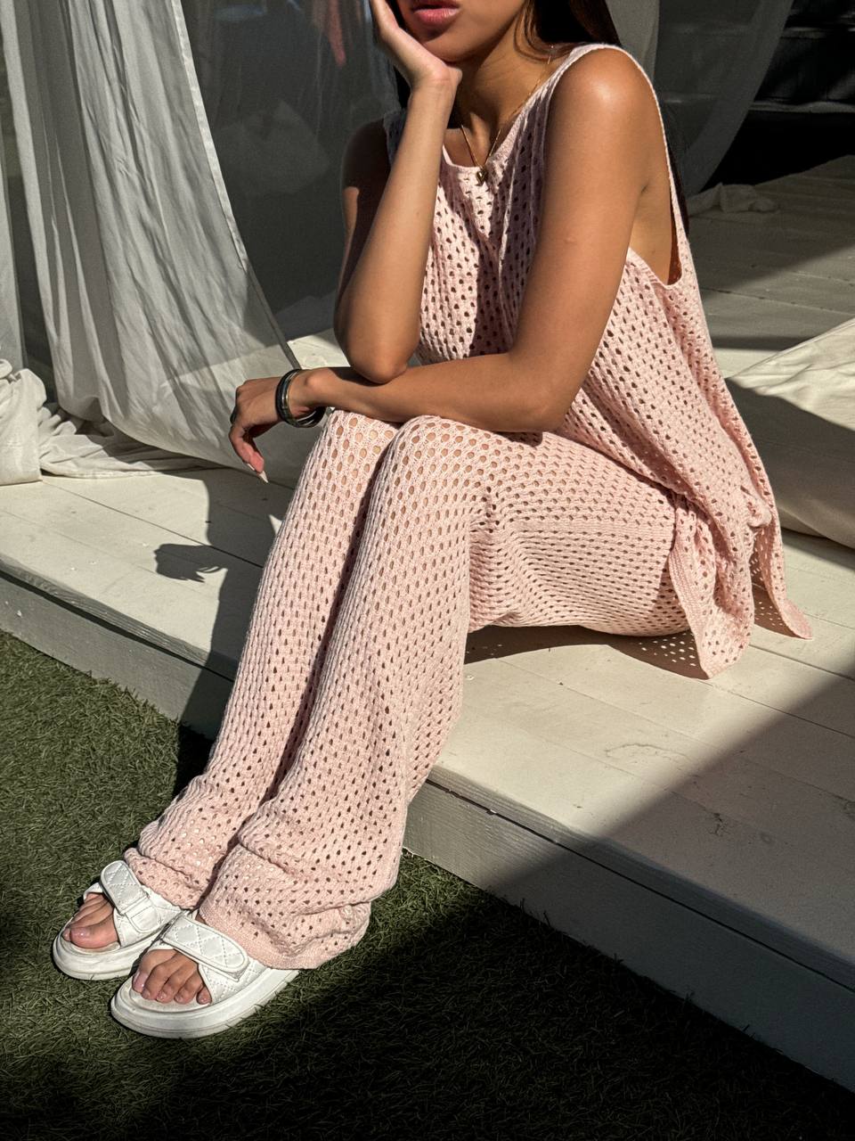 Woman wearing a pink crochet outfit sitting on steps outdoors.