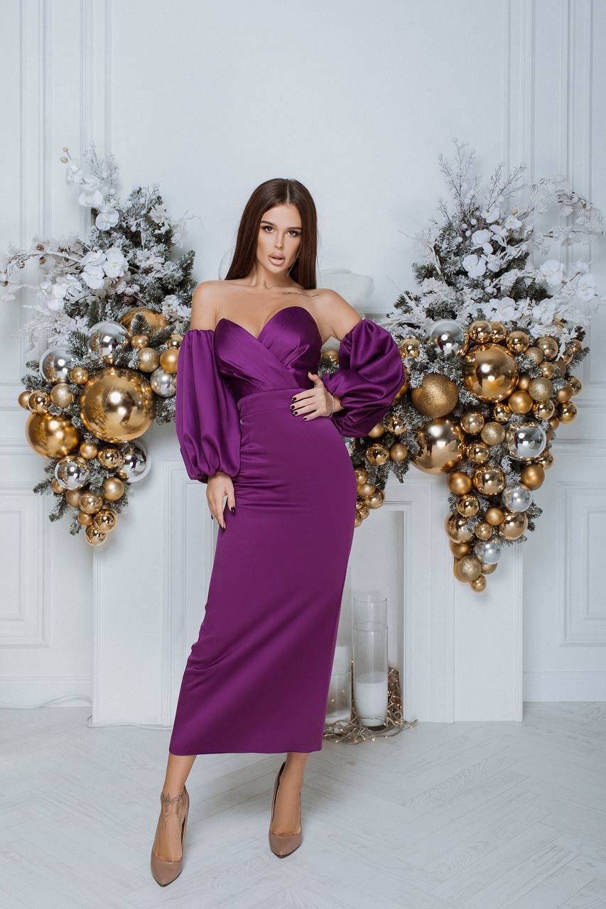 Woman in a purple off-shoulder dress posing in front of decorative Christmas wreaths.