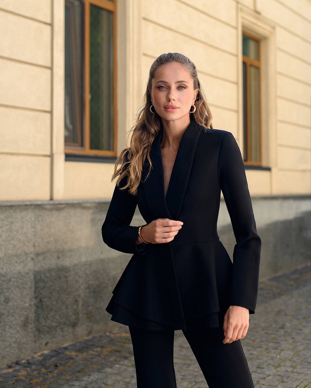 Woman wearing a black peplum jacket standing in front of a building.