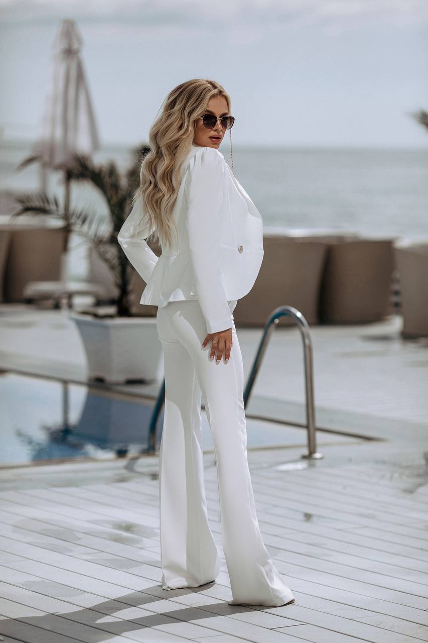 Woman in a white outfit standing on a wooden deck by a pool with ocean view.