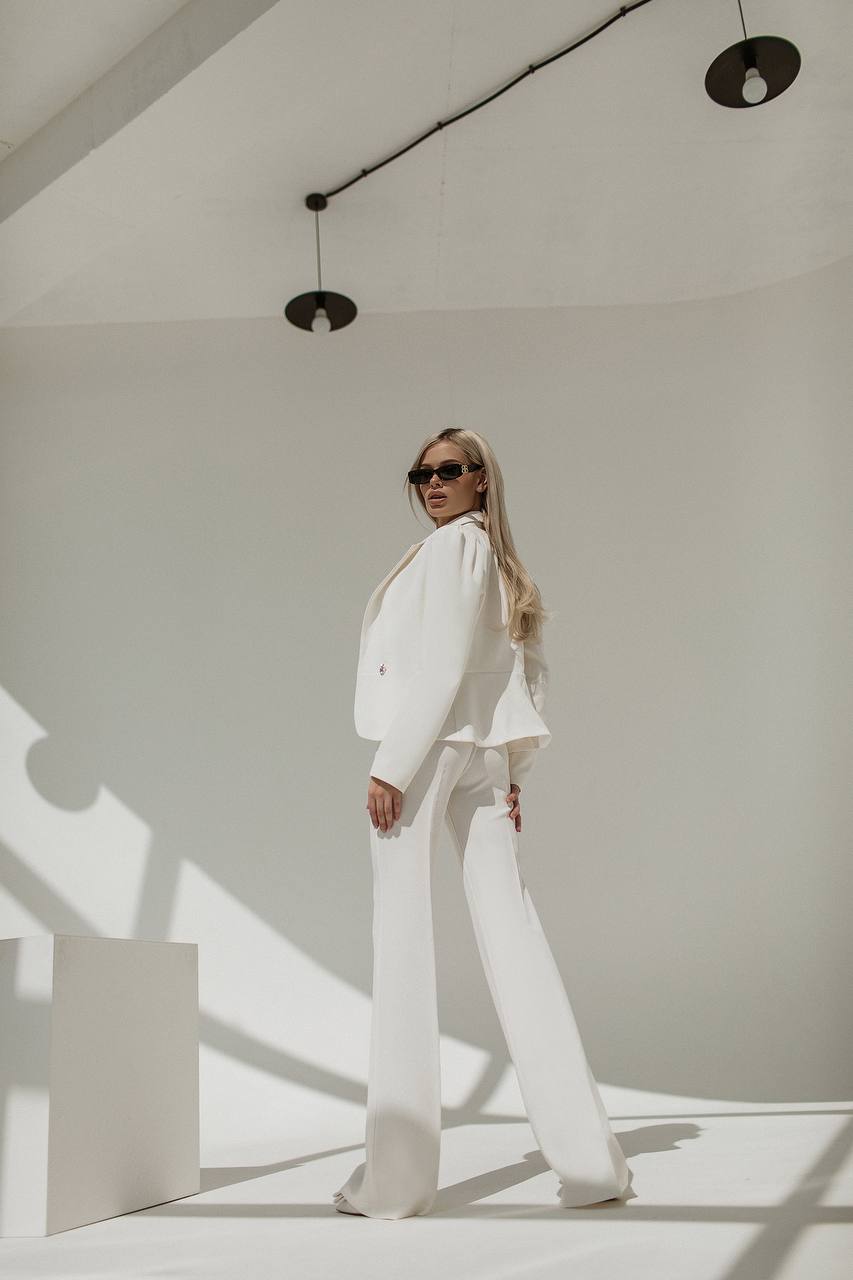 Person wearing a white suit standing in a minimalistic room with white walls and a light fixture.