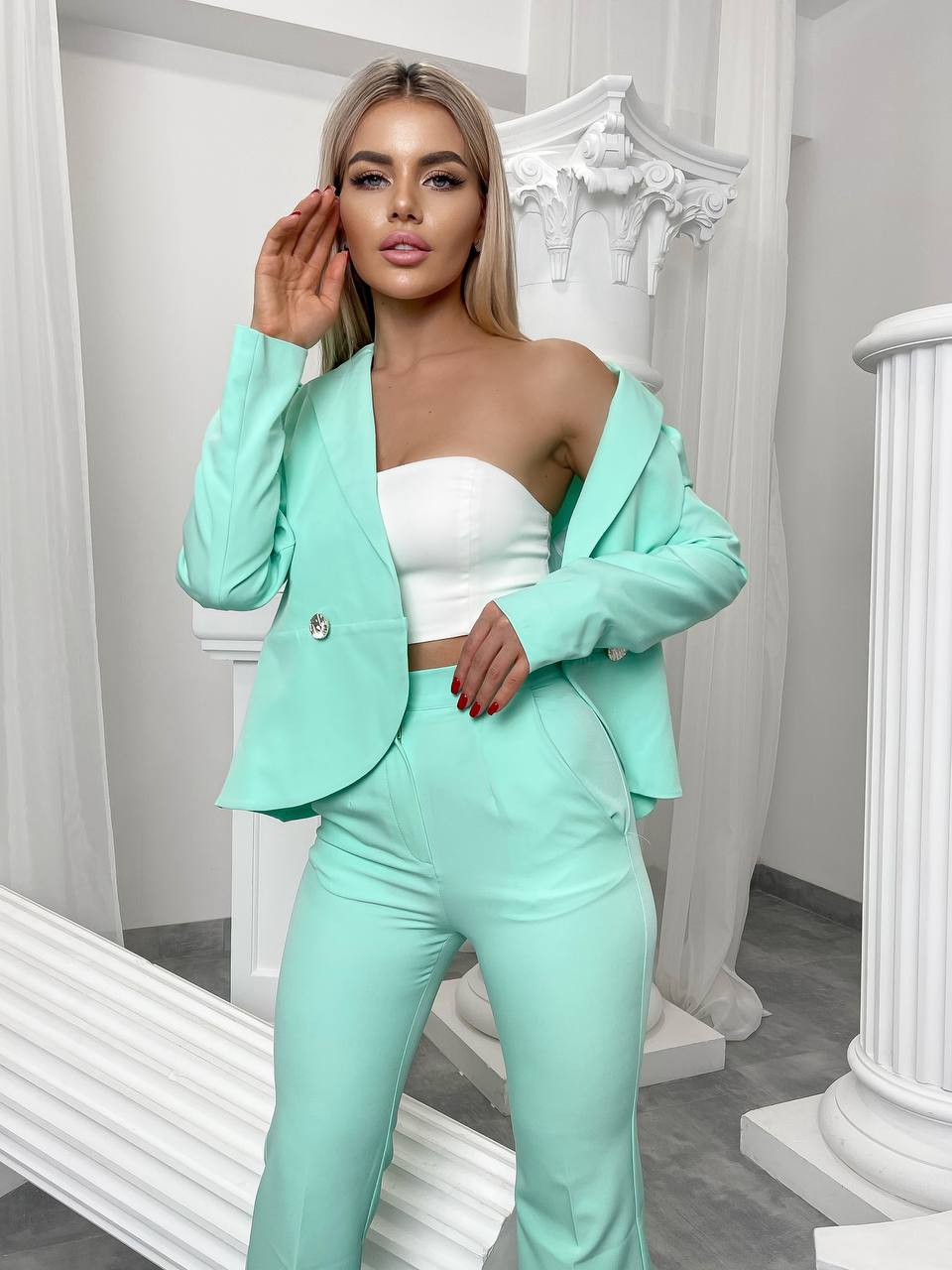 Woman wearing a mint green suit with a white top in an elegant interior setting.