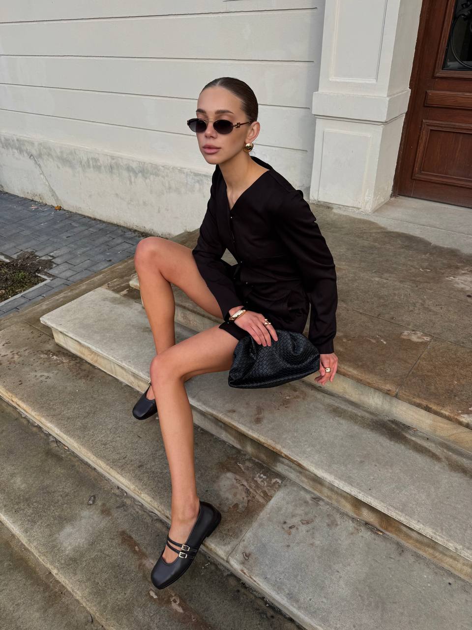 Woman in black outfit sitting on steps wearing sunglasses