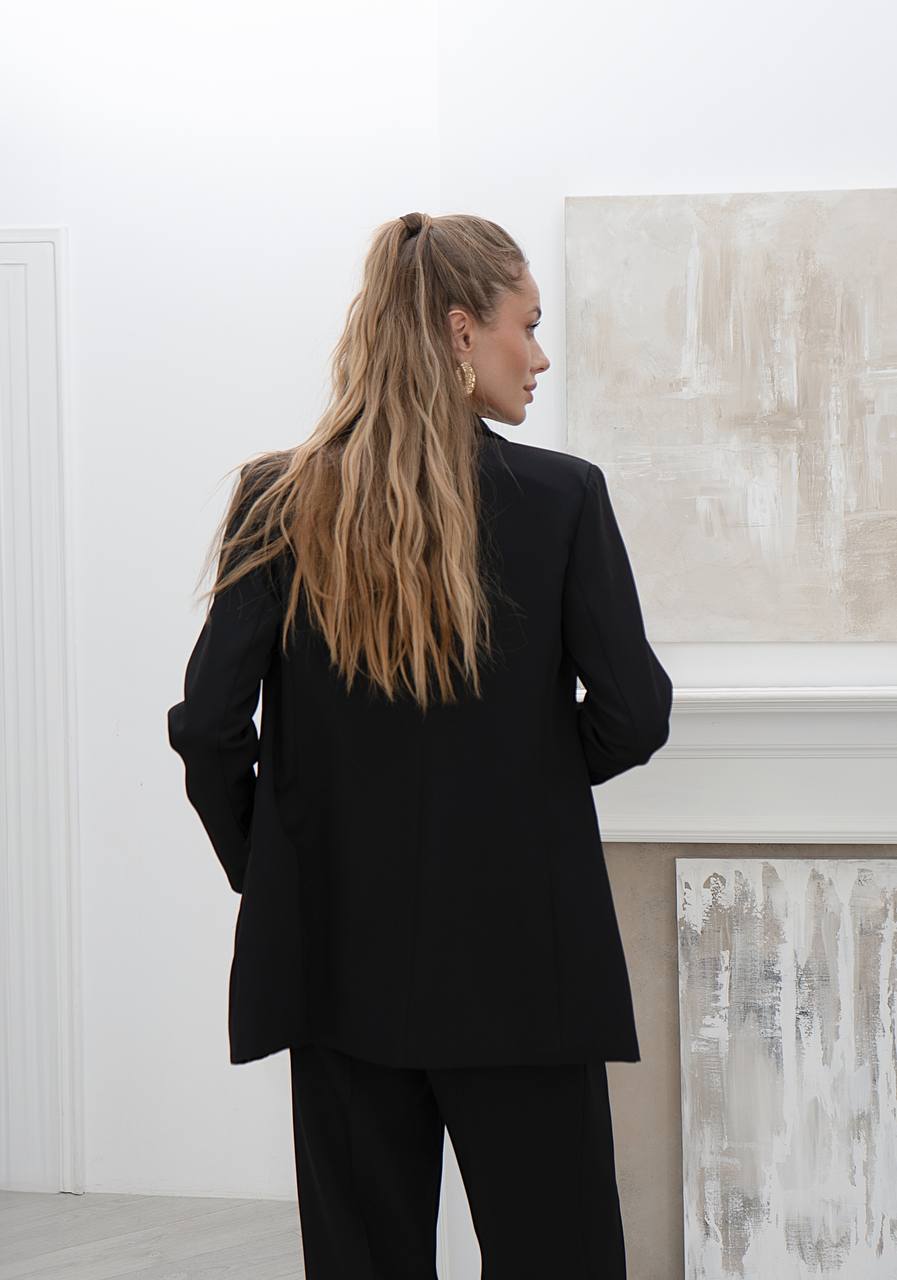Person wearing a black suit standing in a room with abstract art on the wall.