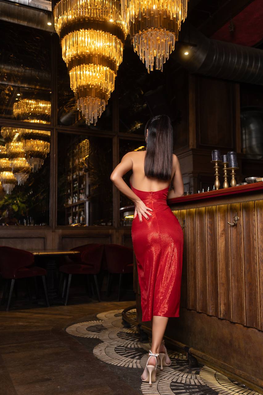 Woman in a red dress standing in a bar with chandeliers hanging above.