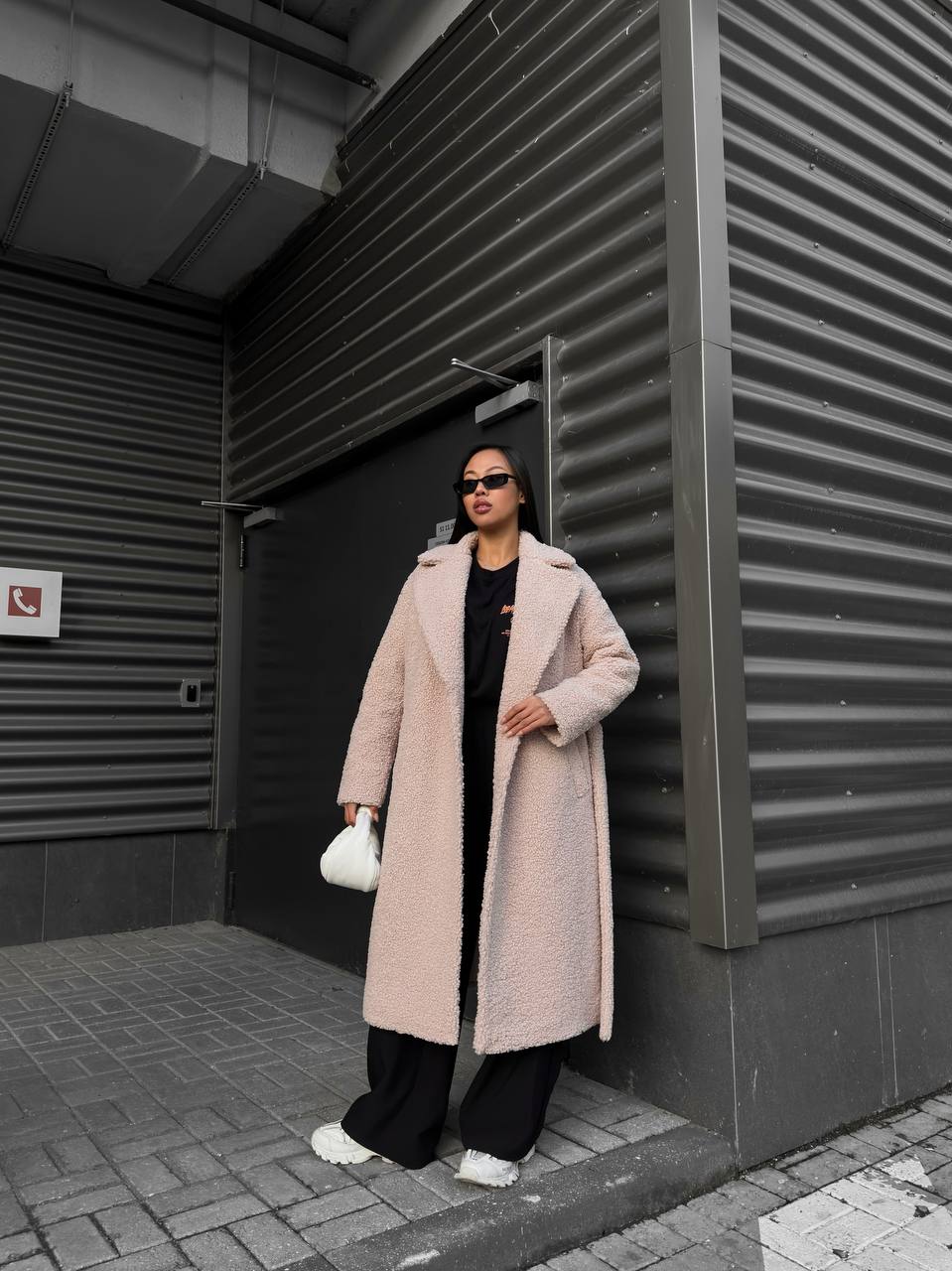 Person wearing a long pink coat standing against a dark wall.