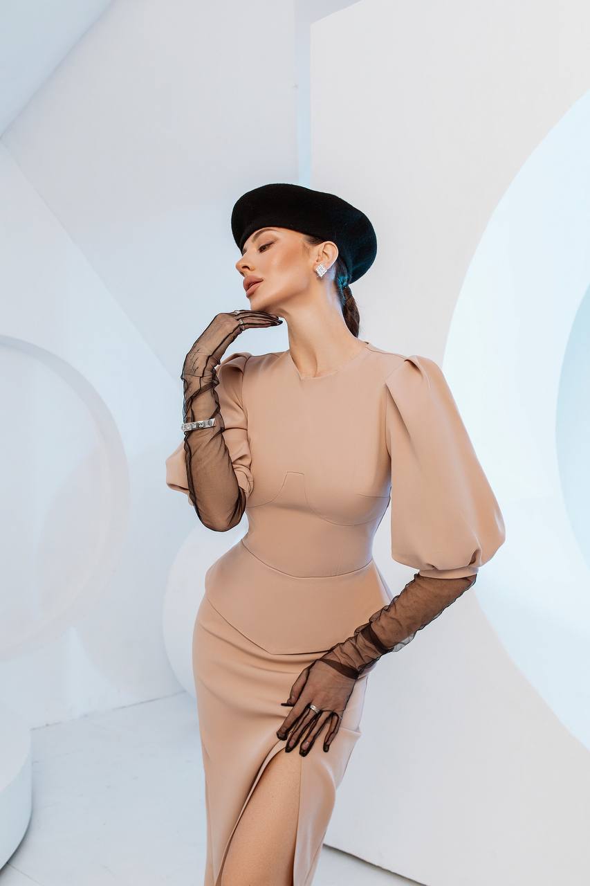 Woman in a beige dress and black hat posing against a white abstract background