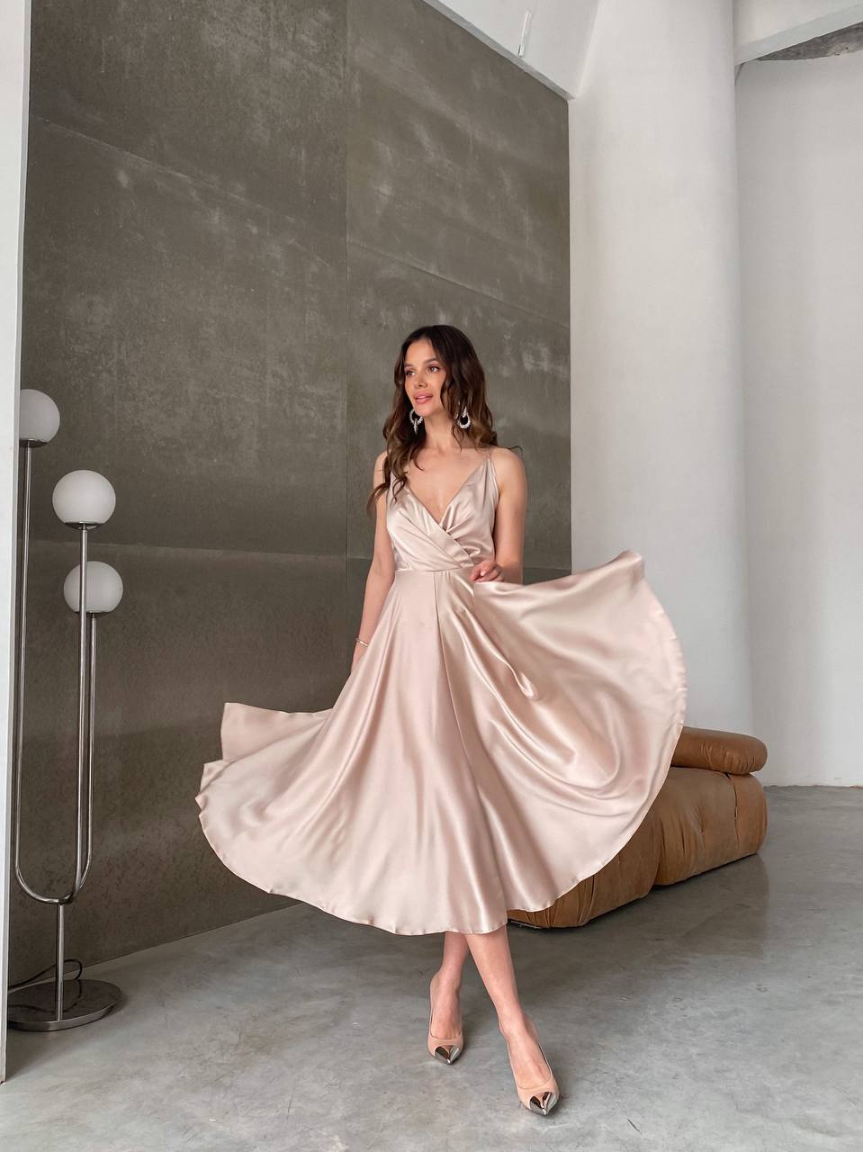 Woman in a pink satin dress standing in a modern room with a gray wall and white floor.