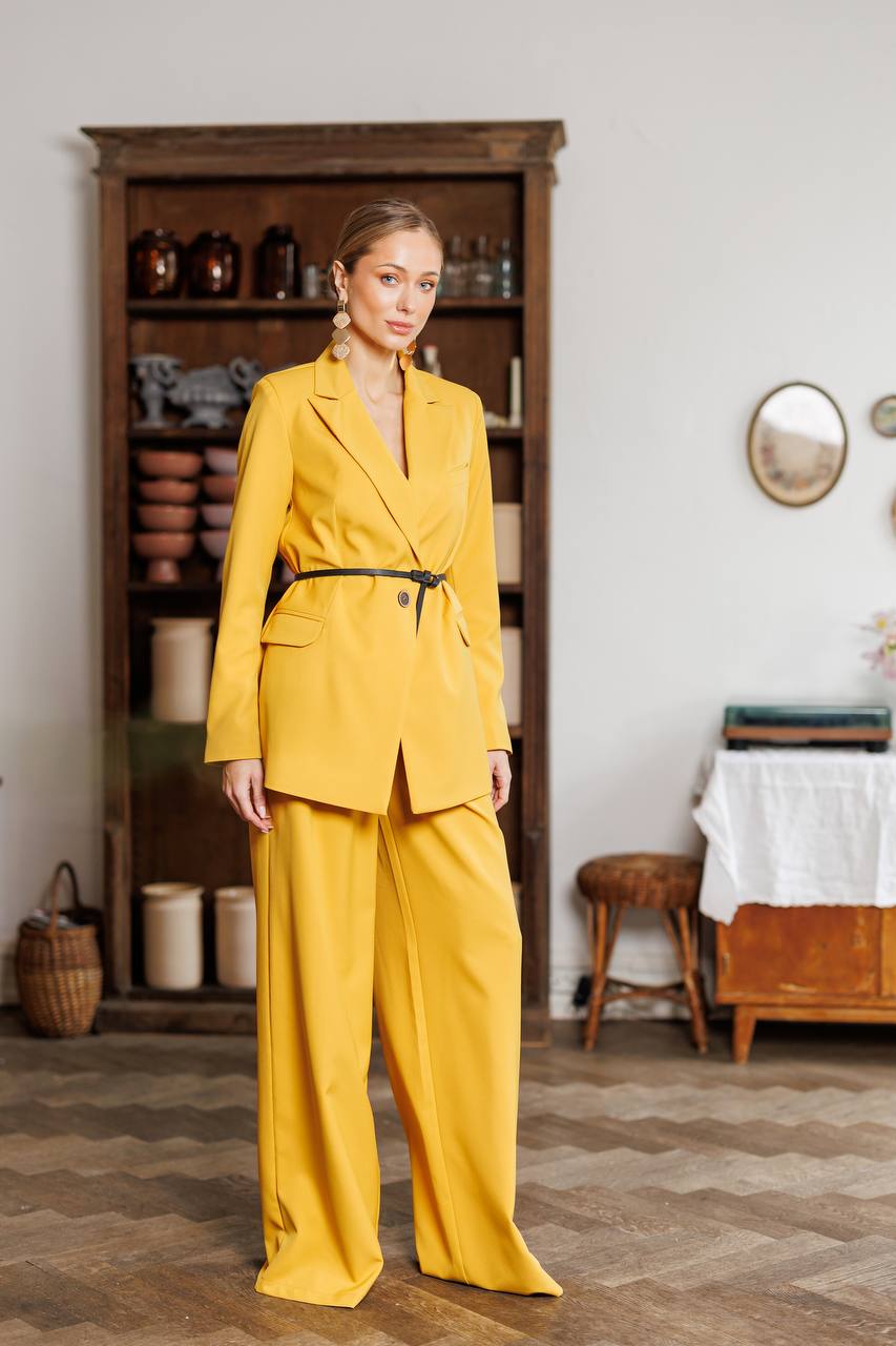 Woman in a yellow suit standing in a room with wooden furniture and decor.