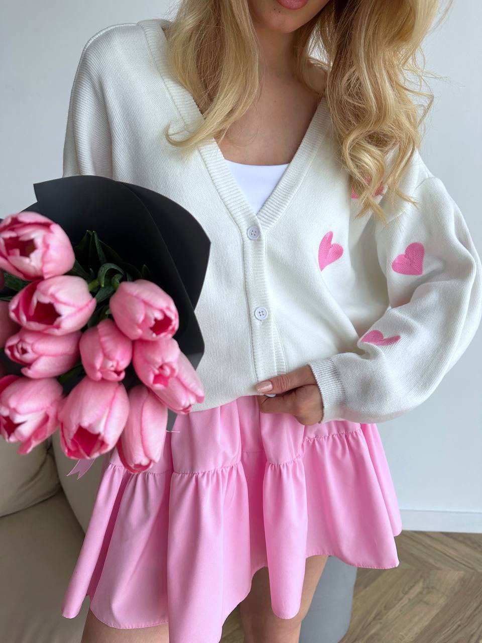 Person wearing a white cardigan with pink hearts and a pink skirt, holding pink tulips.