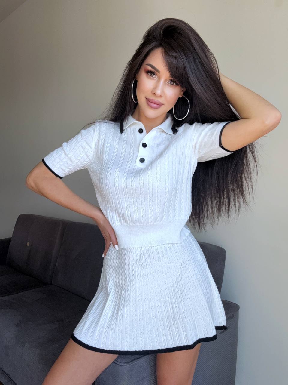 Woman wearing a white dress with black trim posing indoors.
