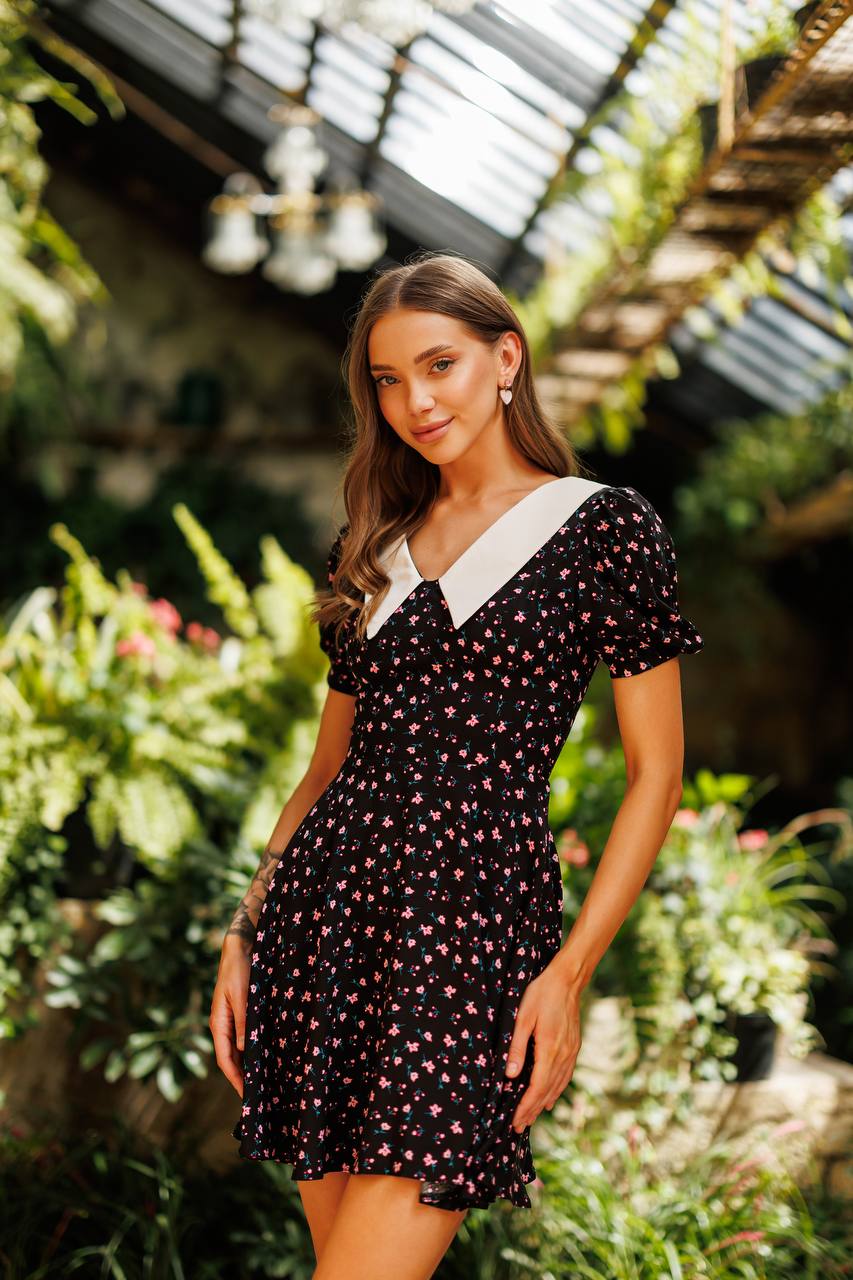 Woman in a black floral dress standing in a garden setting