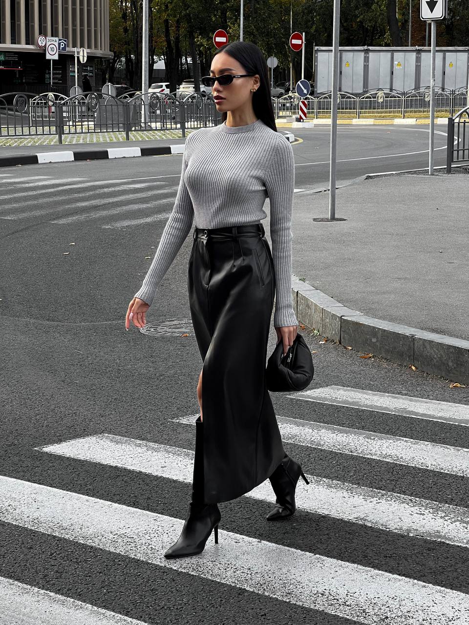 Woman crossing a street wearing a gray sweater and black skirt.