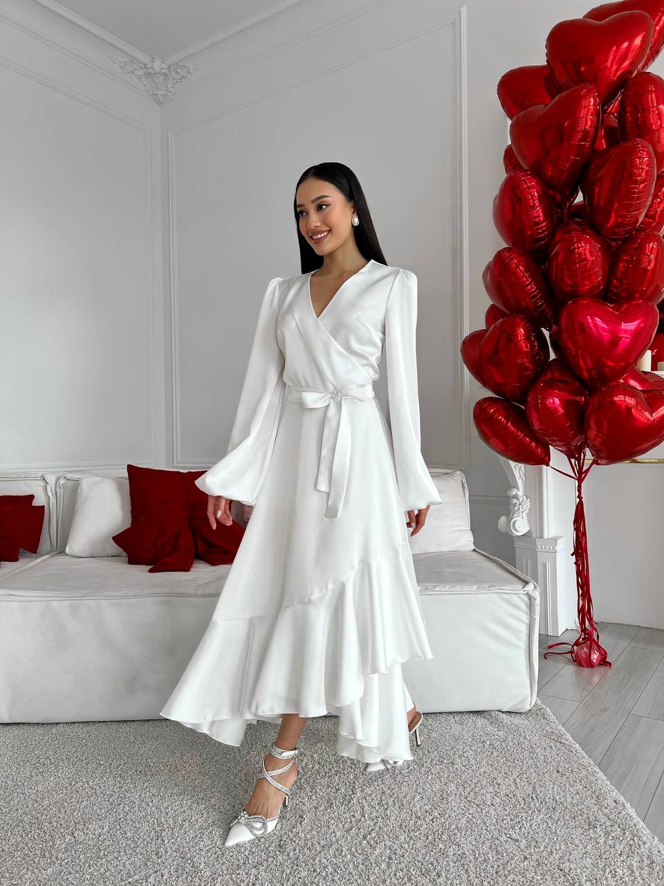 Woman in a white dress standing in a room with red heart balloons.
