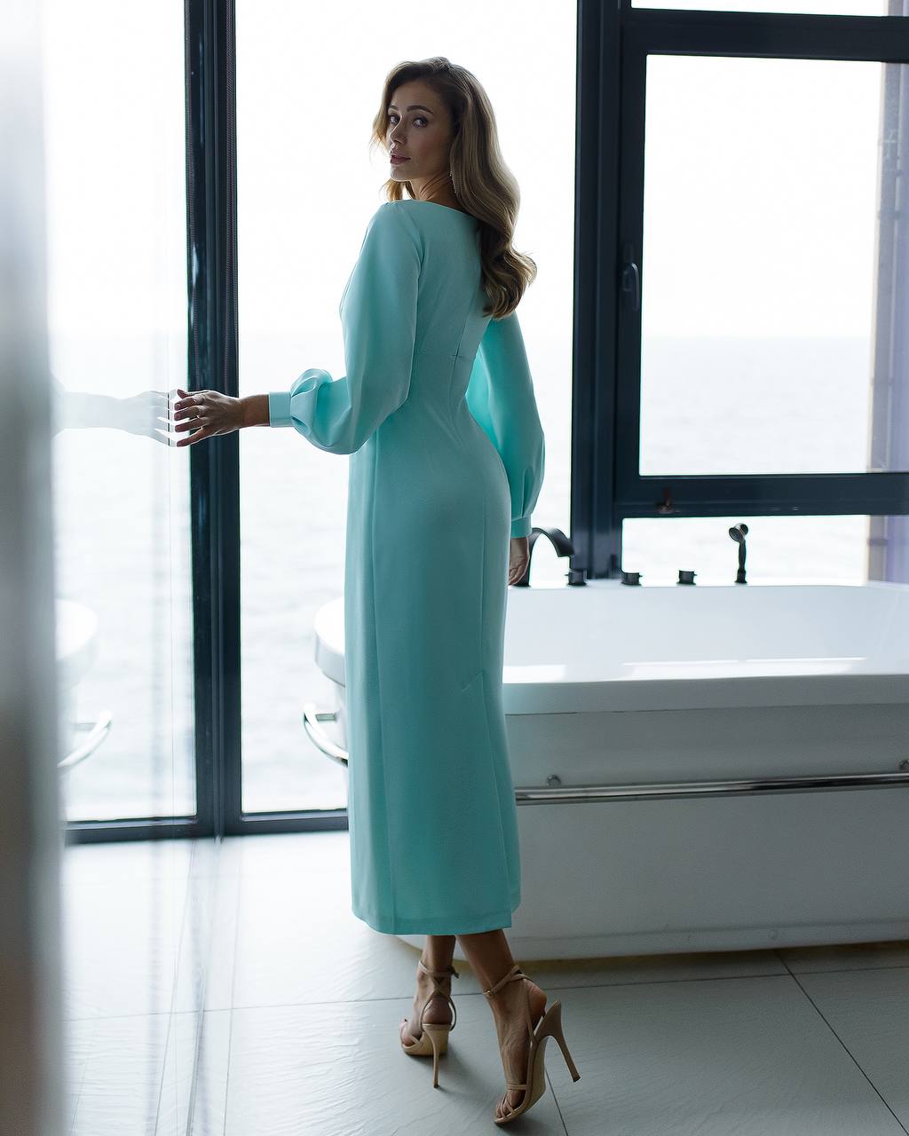 Woman in a turquoise dress standing in a modern bathroom.