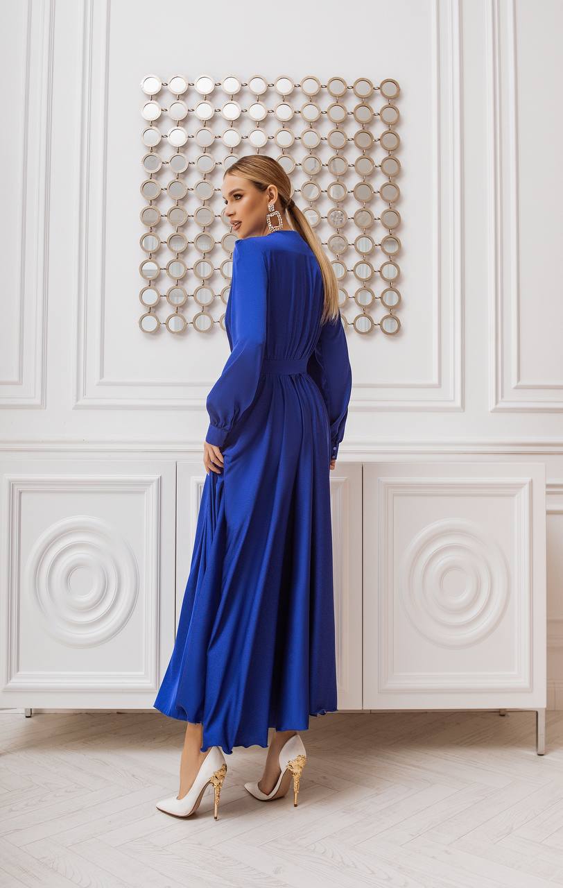 Woman in a blue dress standing in a room with decorative wall art.