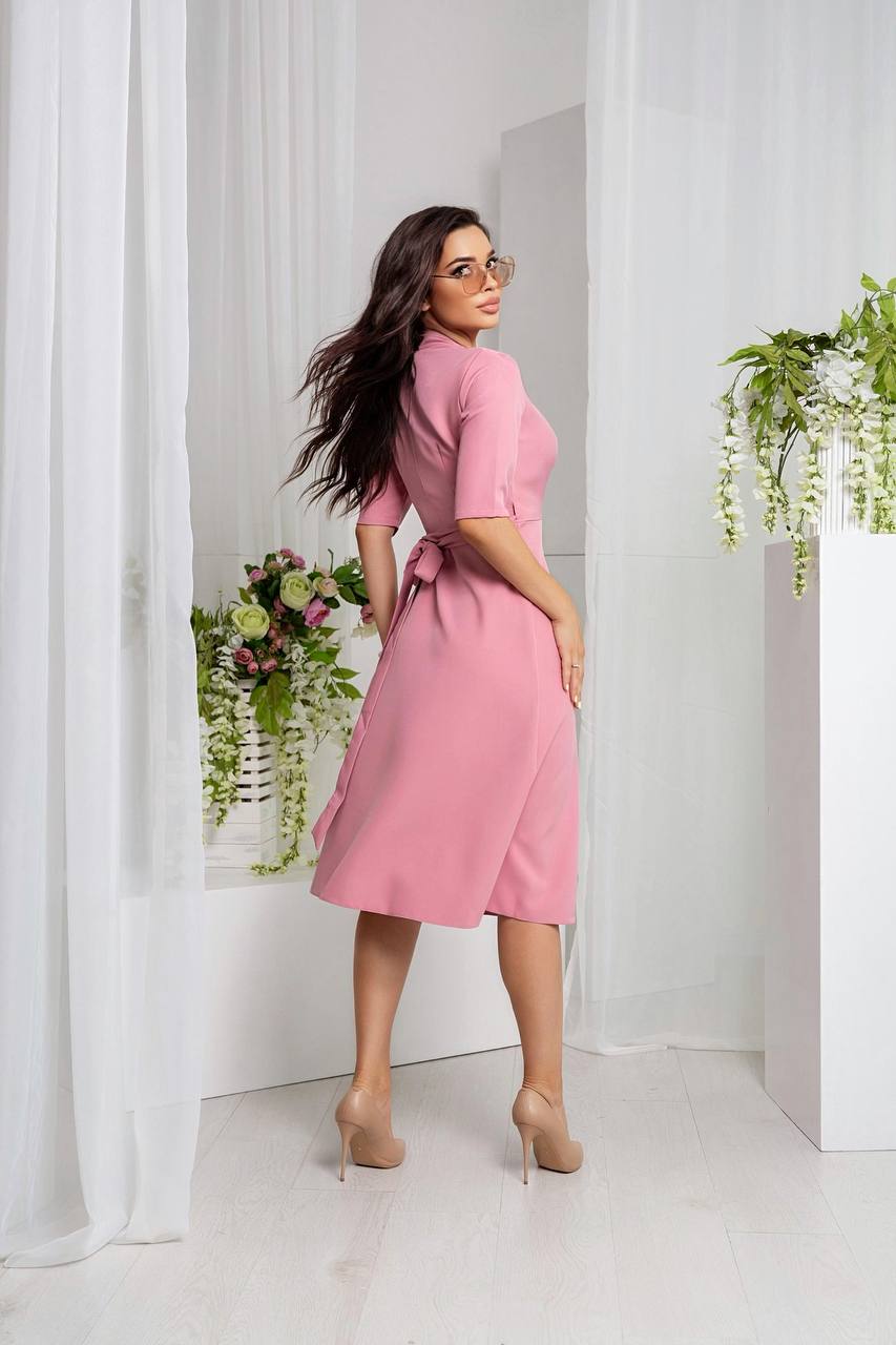 Woman in a pink dress standing in a bright room with white curtains and plants.