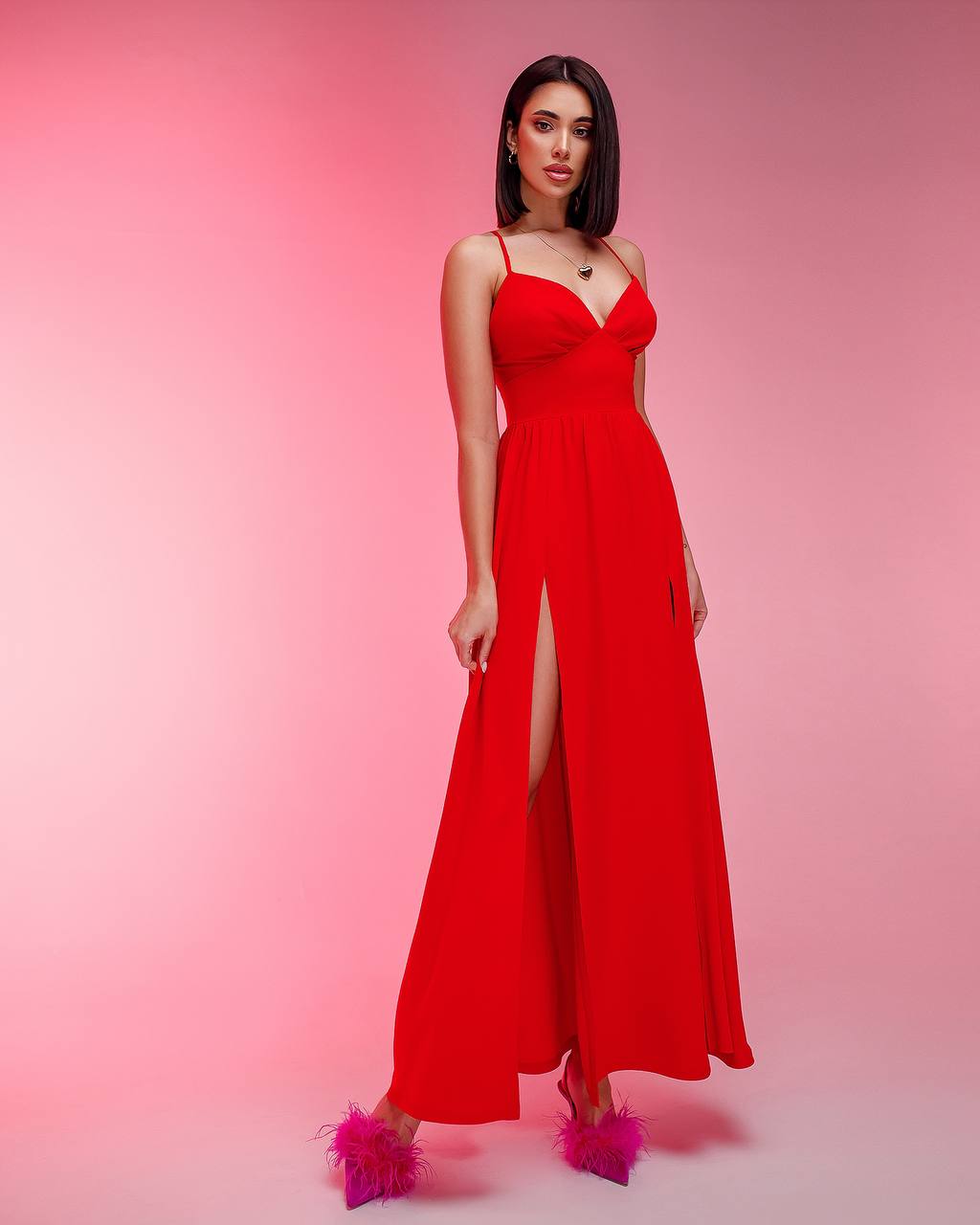 Woman wearing a red dress with a slit on a pink background
