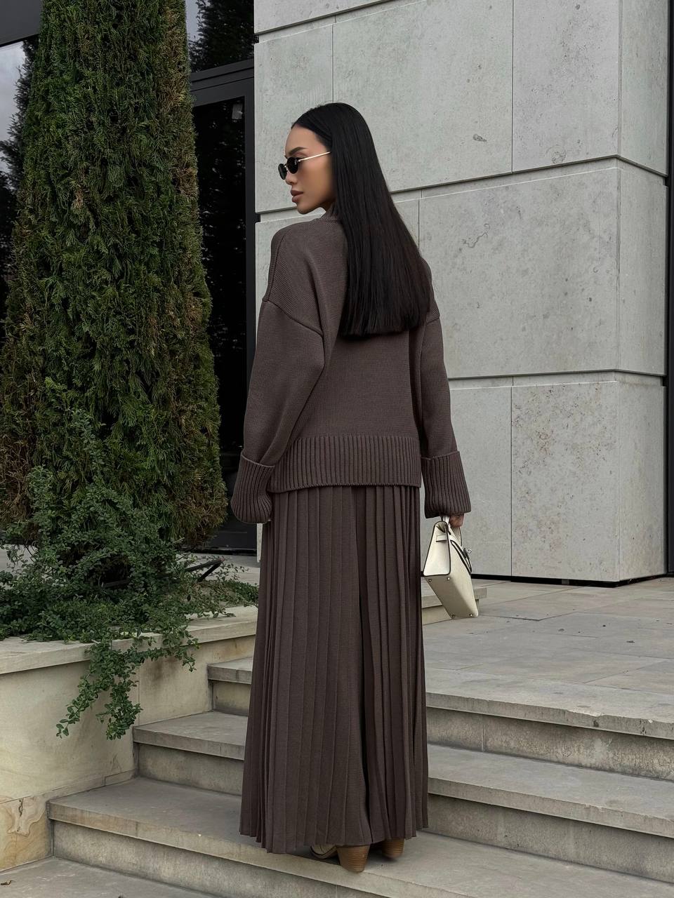 Woman in a brown outfit standing on steps outside a building.
