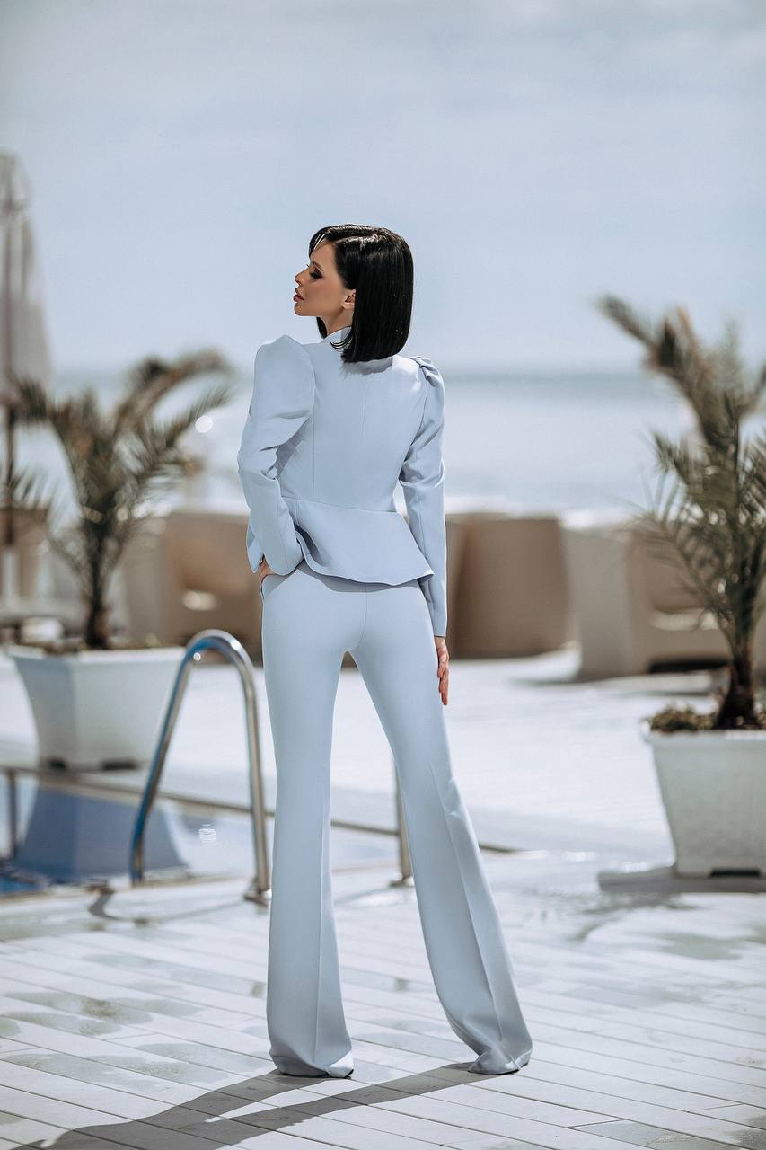 Woman in a light blue suit standing on a rooftop with plants and a pool in the background
