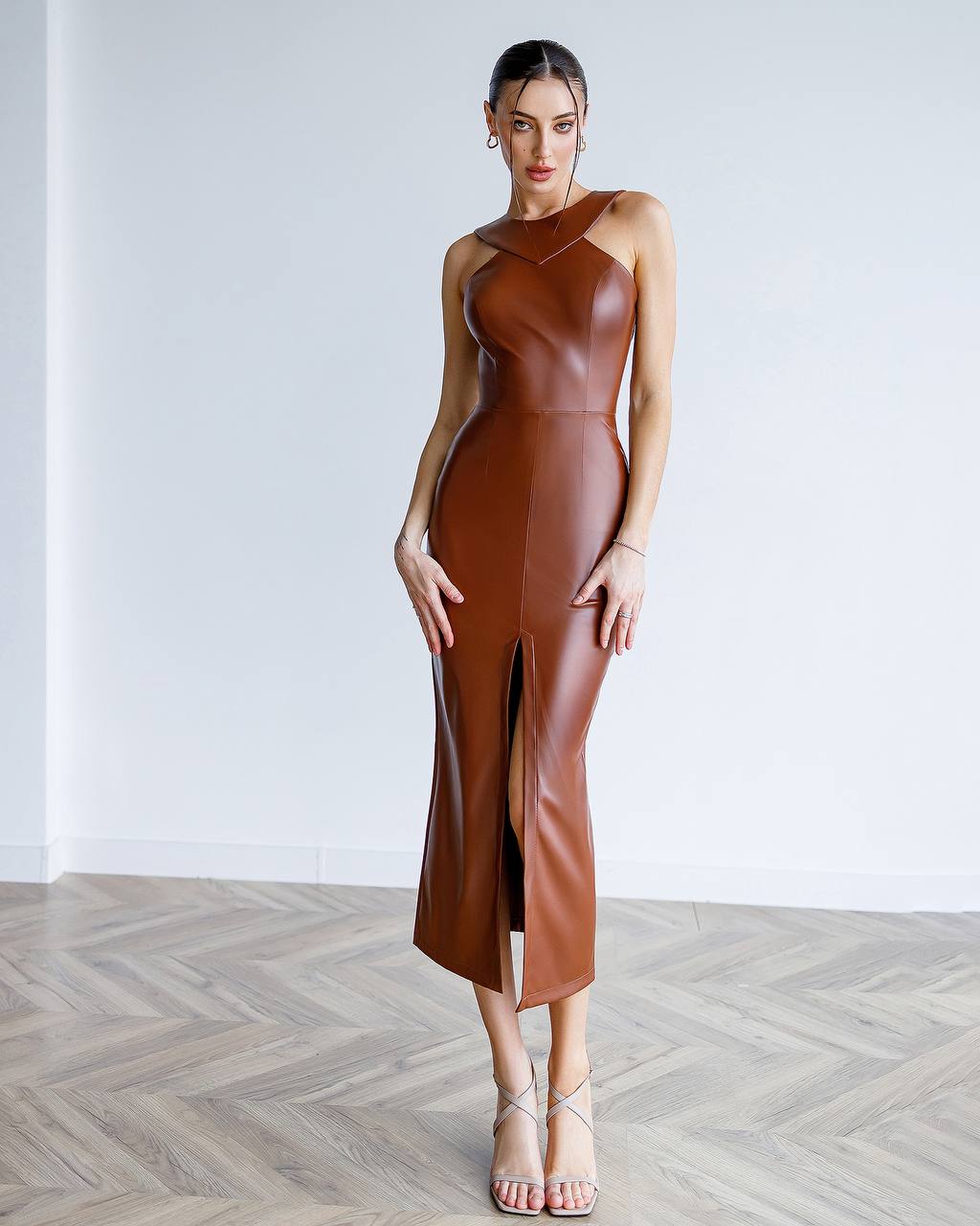 Woman wearing a brown leather dress standing against a white wall.