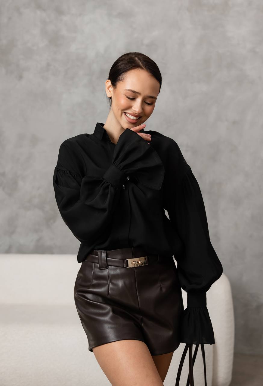 Woman wearing a black outfit with leather shorts against a gray background